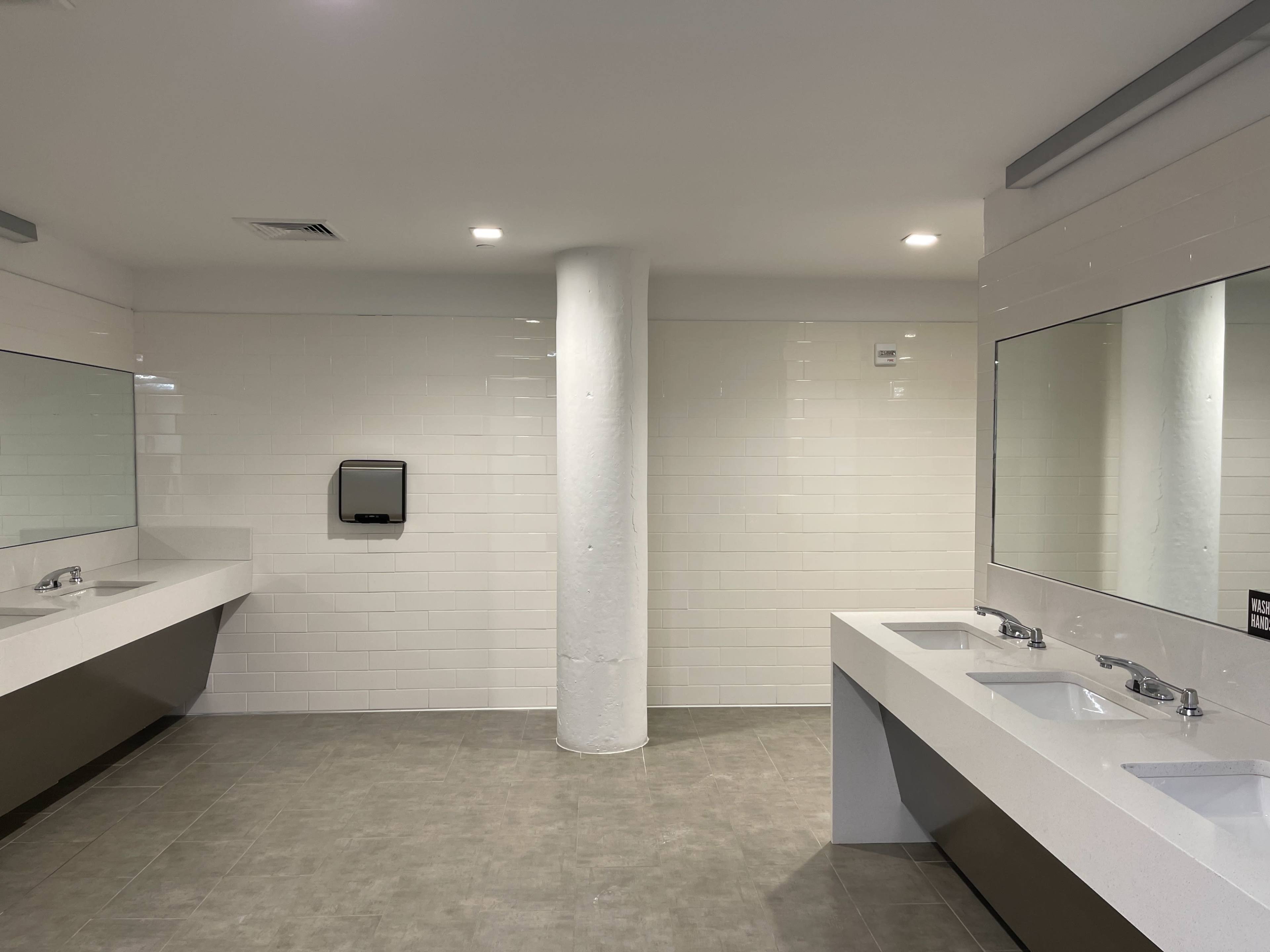 A clean, modern restroom with white tiled walls, dual sinks, and large mirrors.