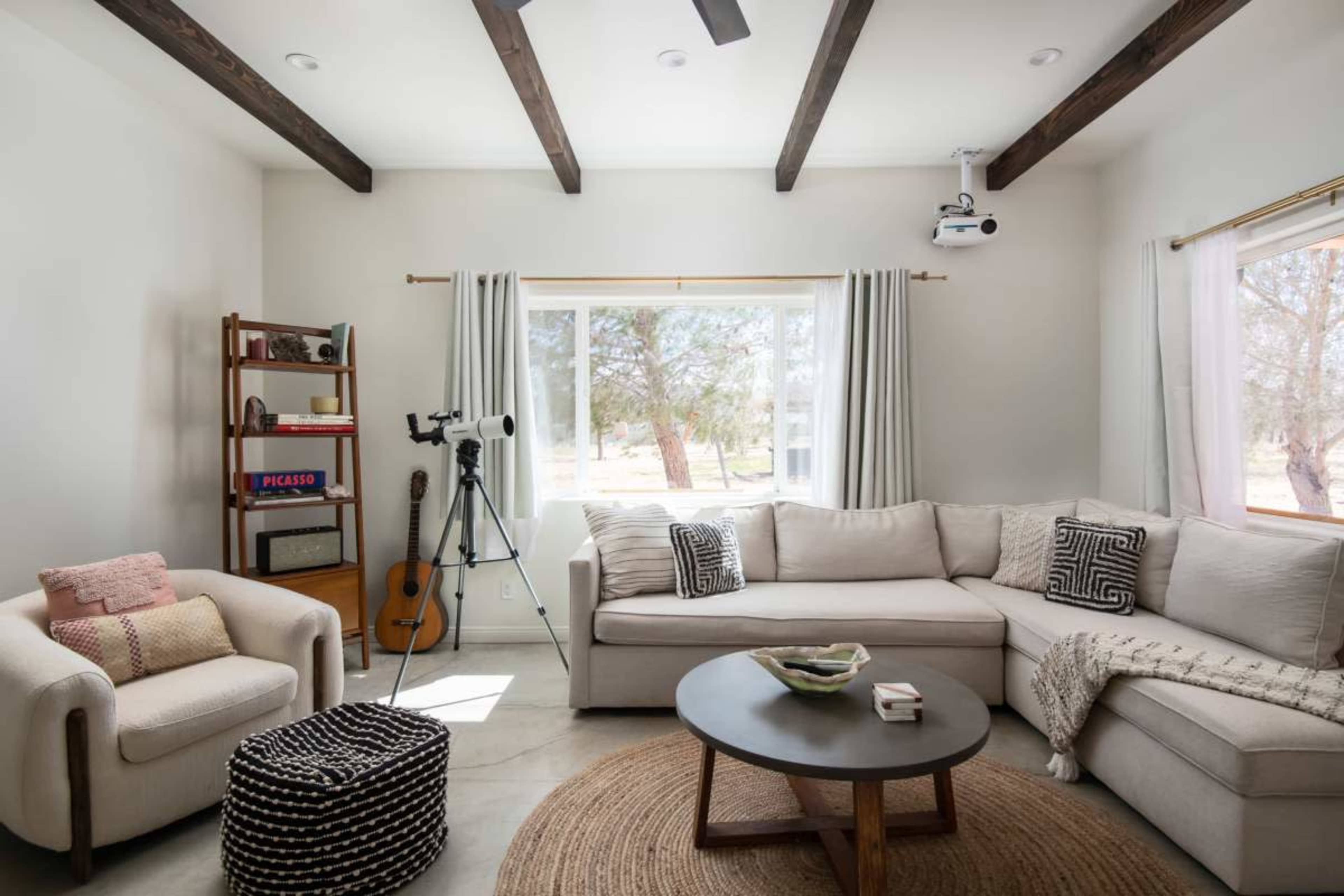 The living room features a large sectional sofa, a telescope, an acoustic guitar, and a round coffee table placed on a circular rug.