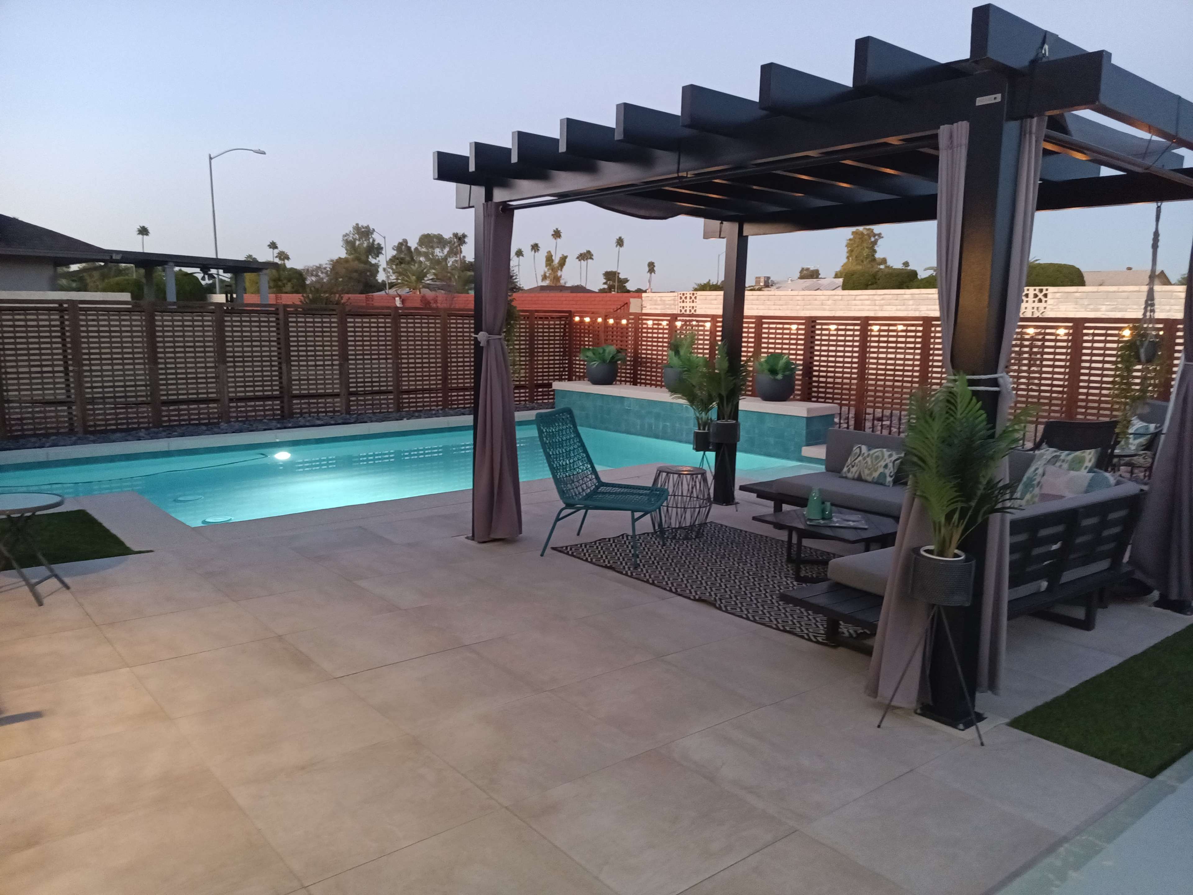 A modern outdoor space featuring a pool, a pergola with seating, and surrounding landscaping.