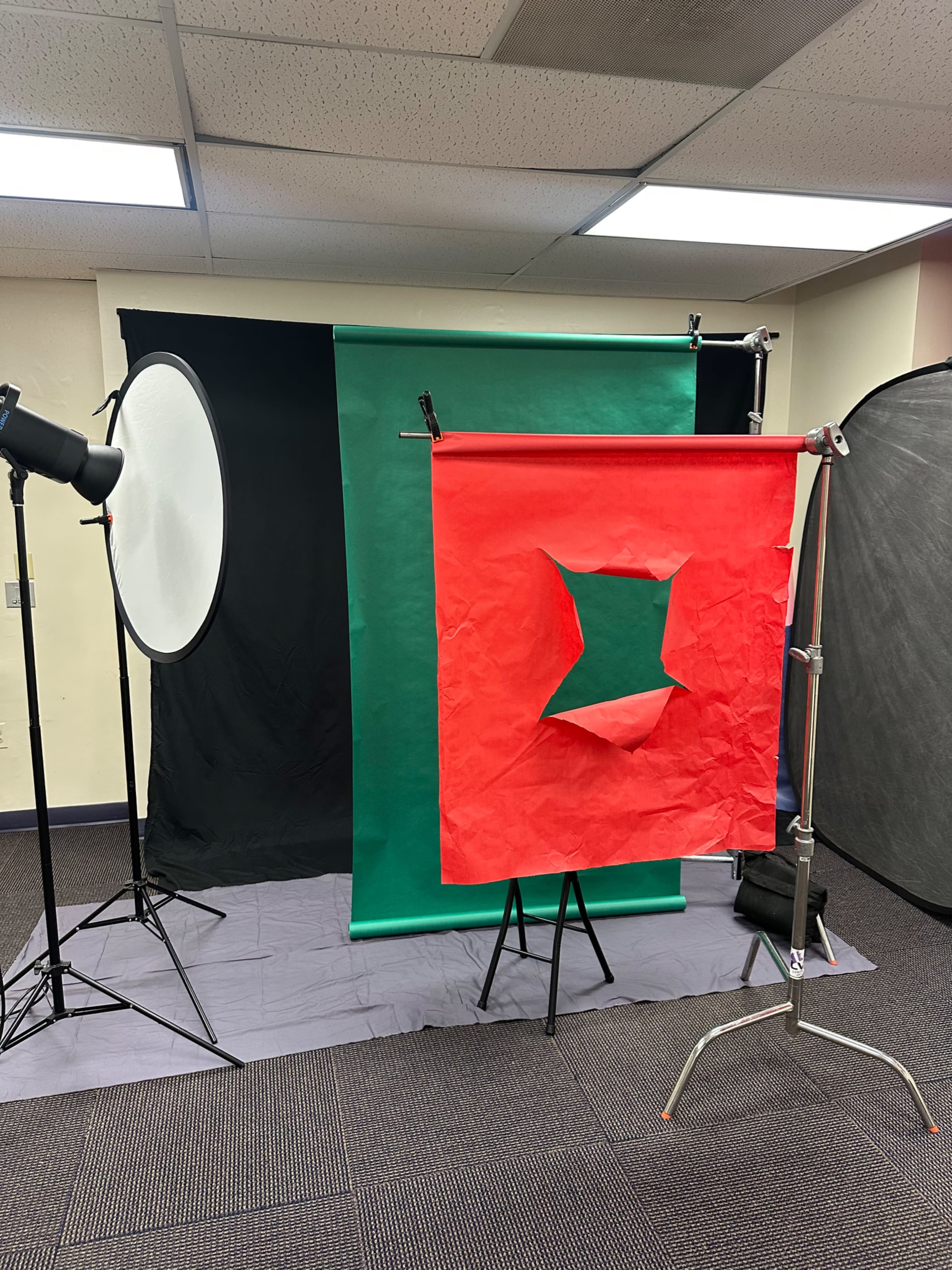 The image shows a photography studio setup with green and red backdrops, lighting equipment, and a gray floor covering.