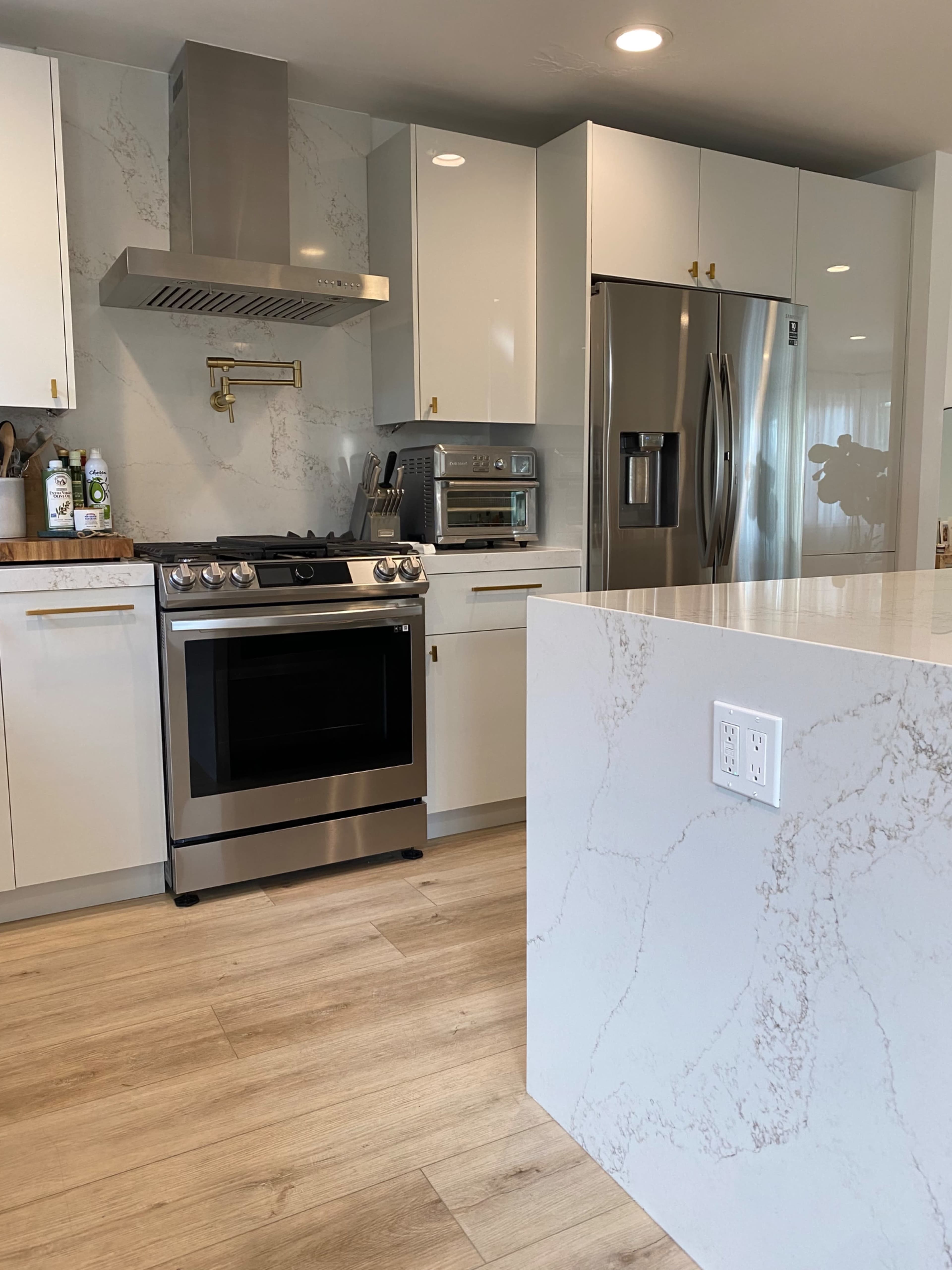 A modern kitchen features a stainless steel oven, sleek white cabinetry, and a large marble countertop.