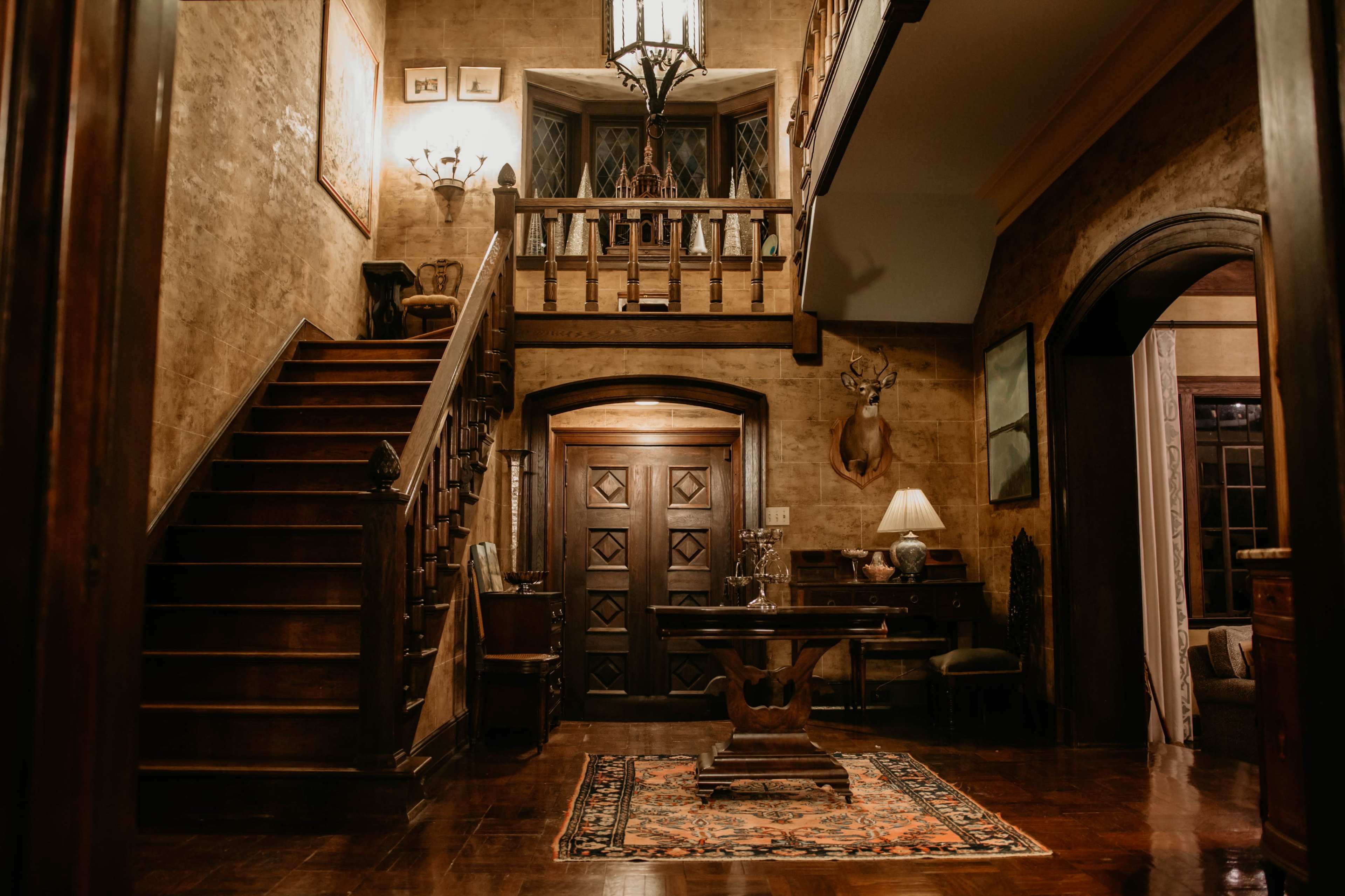 An interior of a wooden foyer with a staircase leading to a second level, wooden doors, and a decorative rug on the floor.