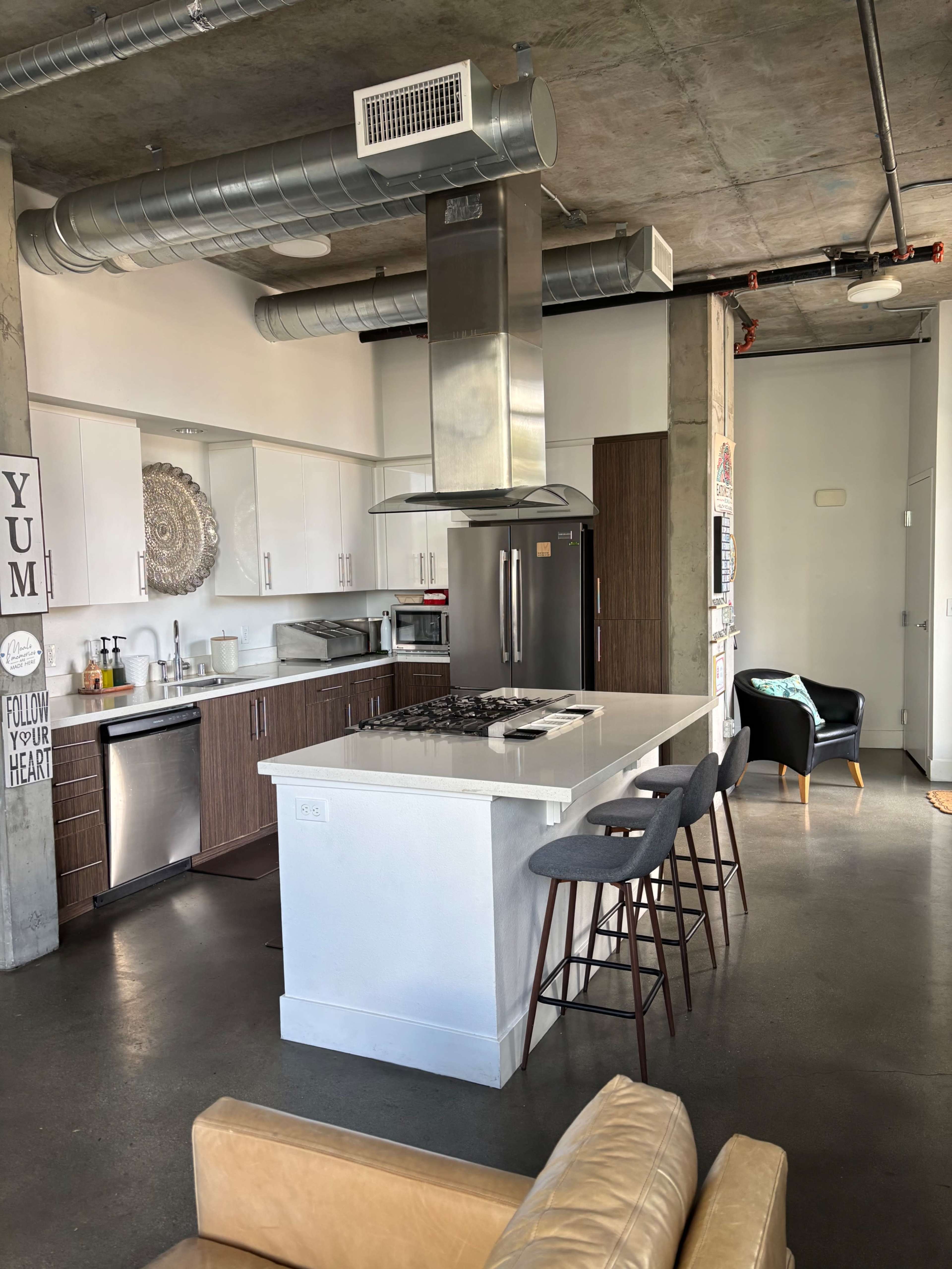 The image shows a modern kitchen with a central island, stainless steel appliances, and a seating area with bar stools.