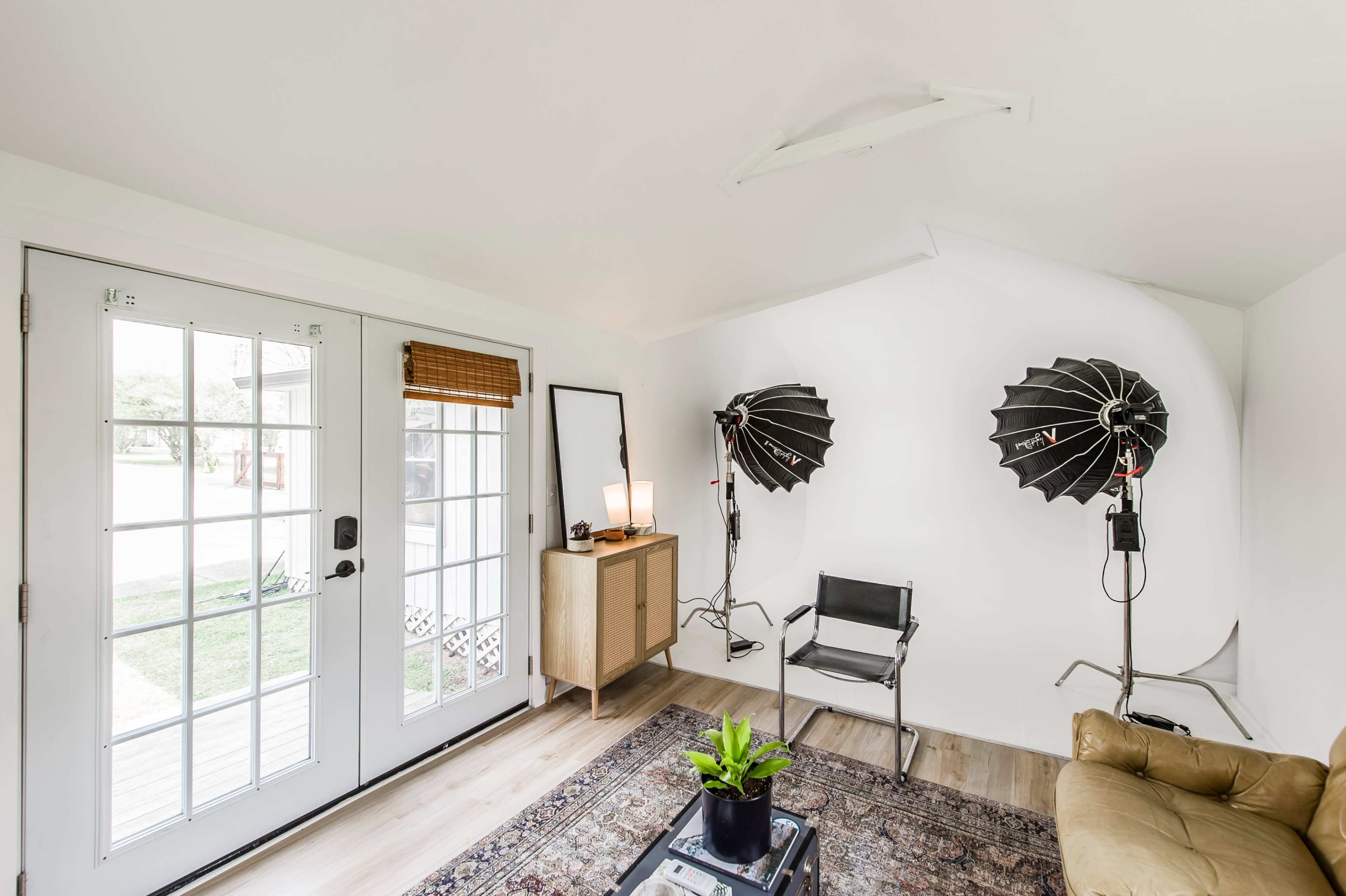The image shows a photo studio with two lighting setups, a chair, a cabinet, a mirror, and glass doors leading to an outdoor area.