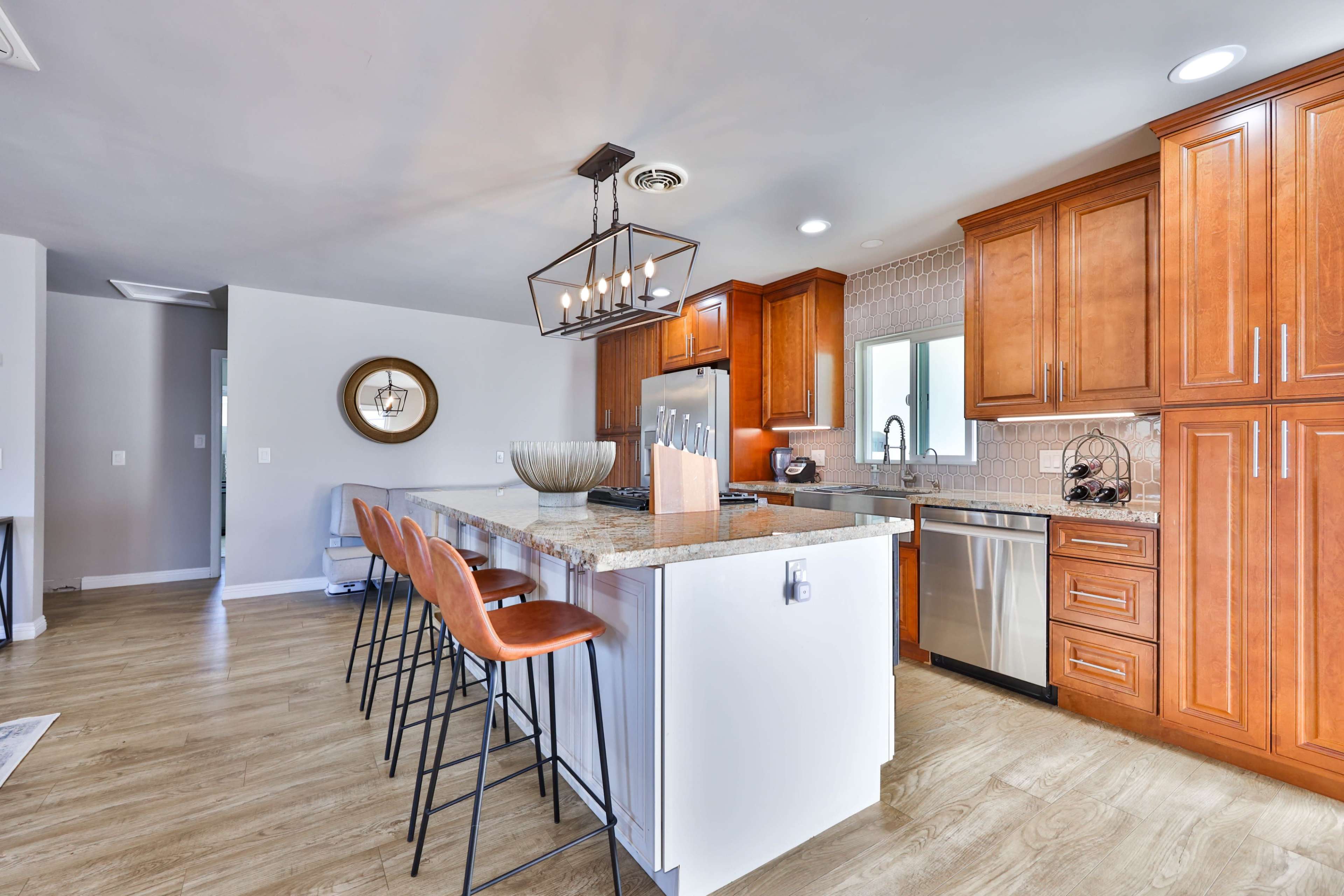 A modern kitchen features wooden cabinets, a large island with bar stools, and stainless steel appliances.