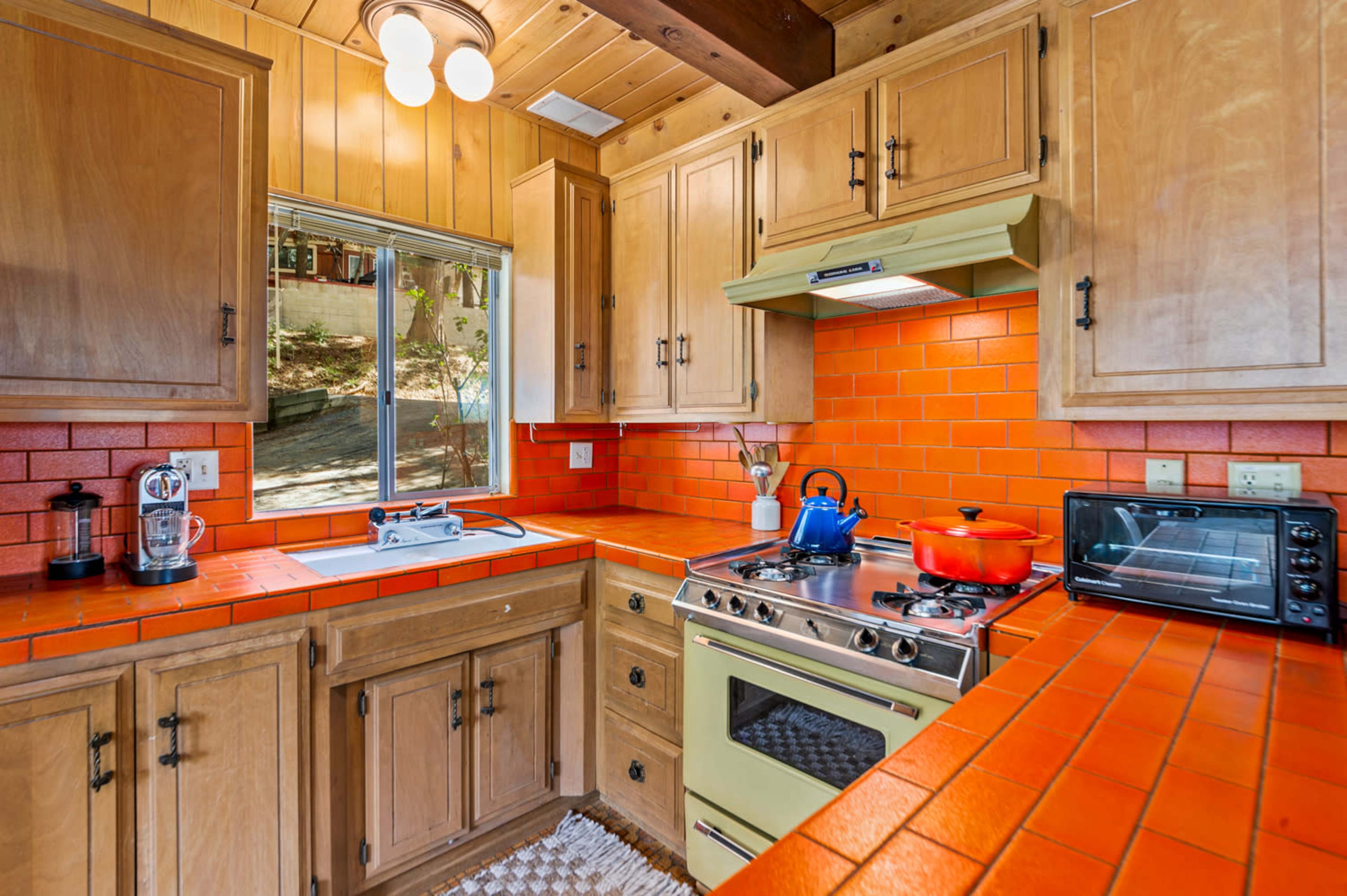 The kitchen features wooden cabinets, orange tile countertops, and a window overlooking a landscaped area.