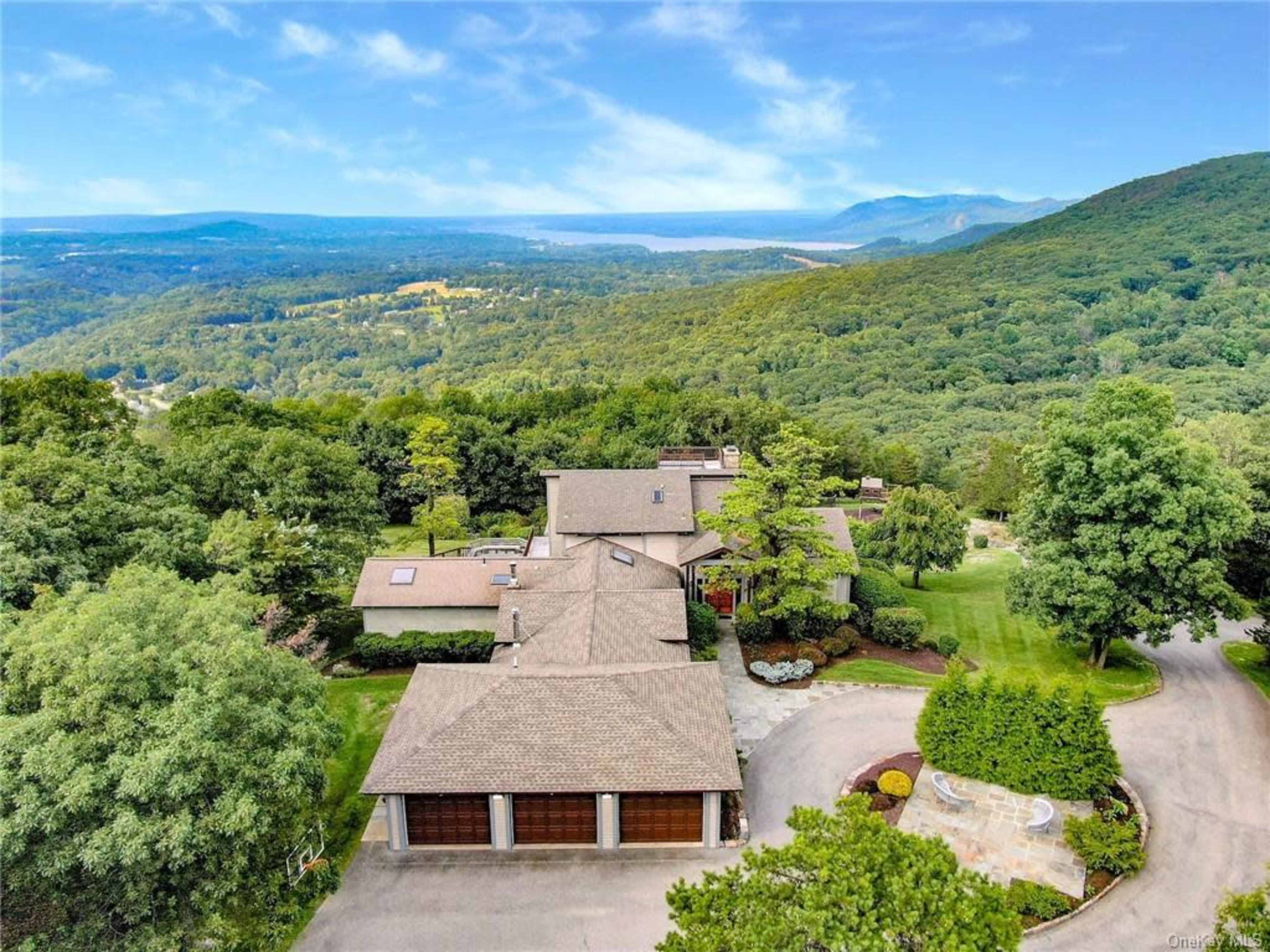 A large modern house set in a lush, green landscape with rolling hills and a distant view of mountains.