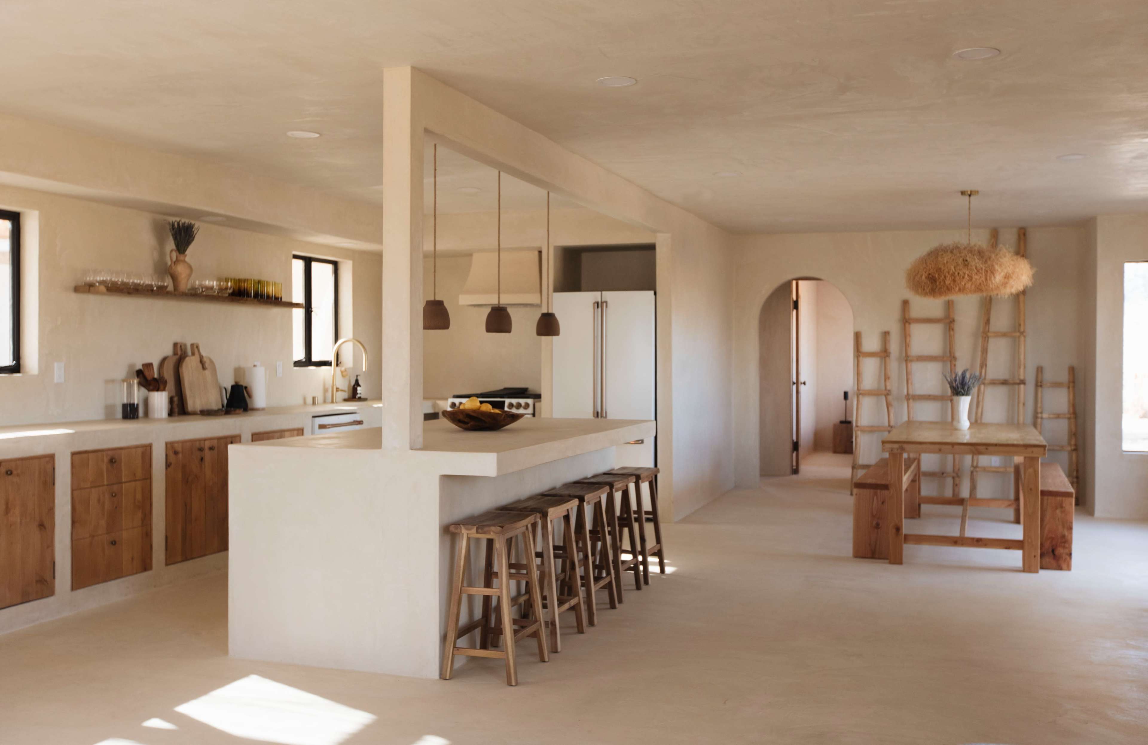 A spacious, minimalist kitchen features wooden cabinetry, a large island with bar stools, and a dining area with a wooden table in an open layout.