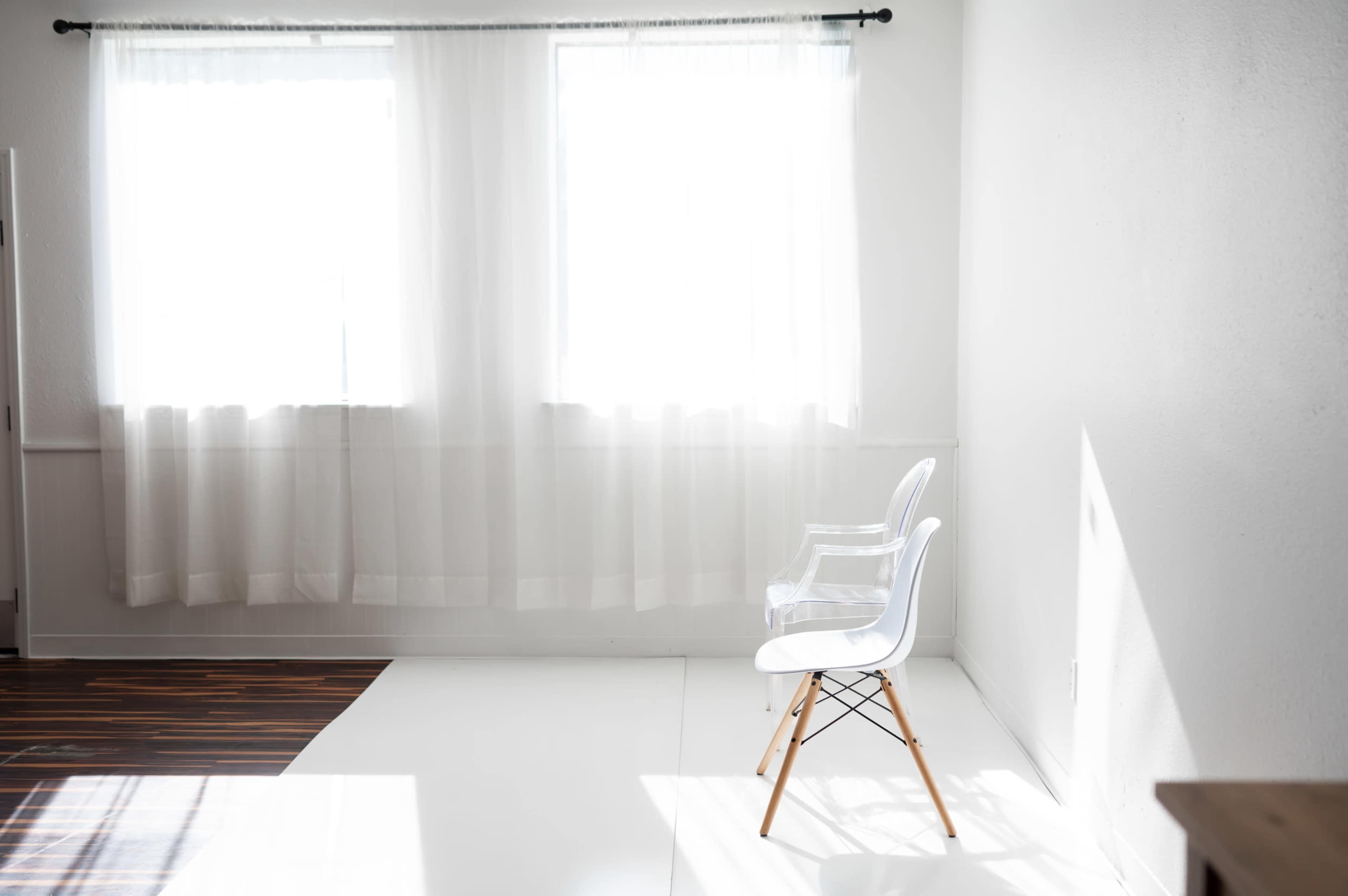 A bright, minimalistic room with two transparent chairs near windows covered by sheer white curtains.
