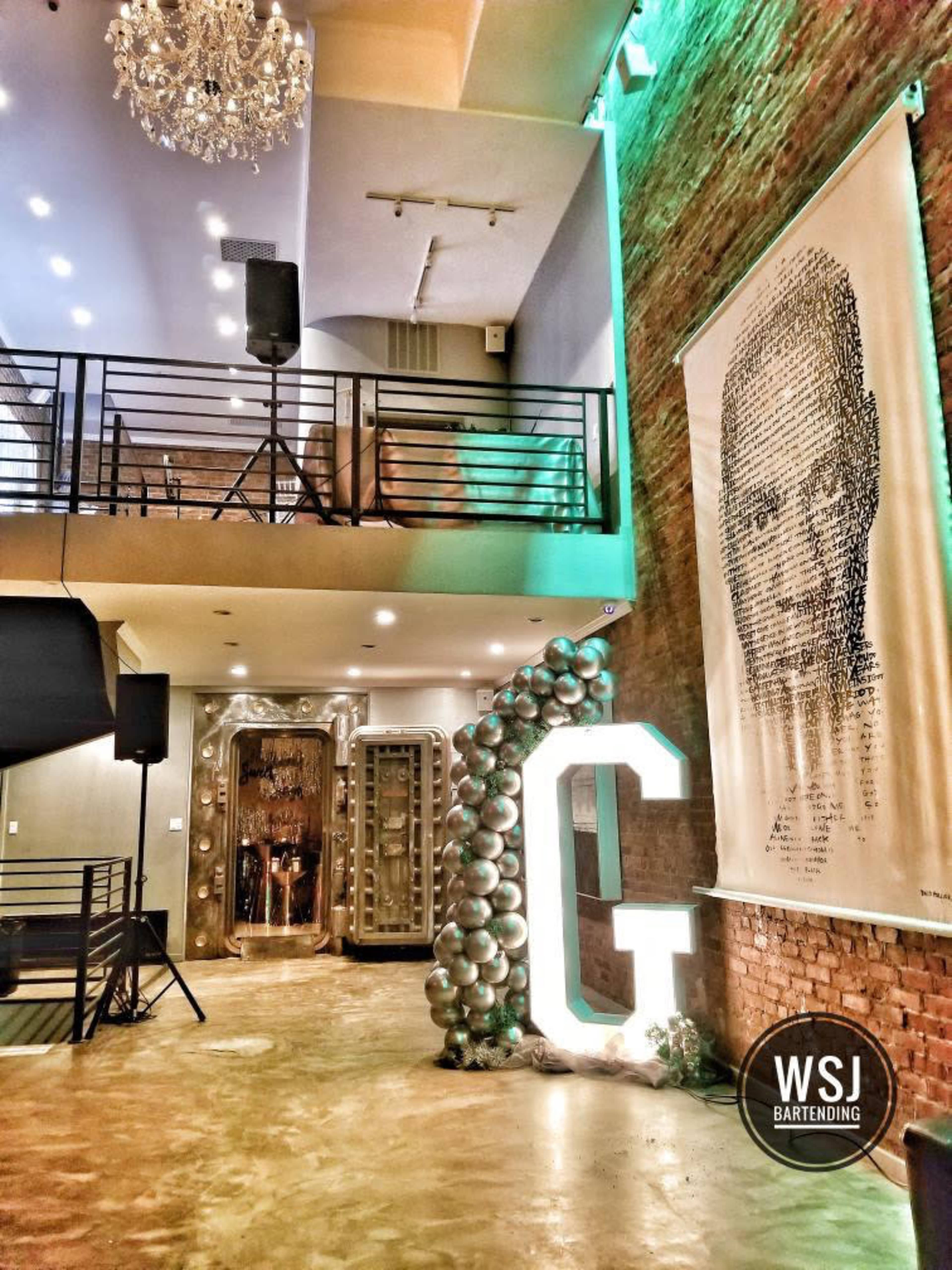 The interior features a two-level space with a large illuminated letter "G," balloon decorations, and a prominent mural on a brick wall.