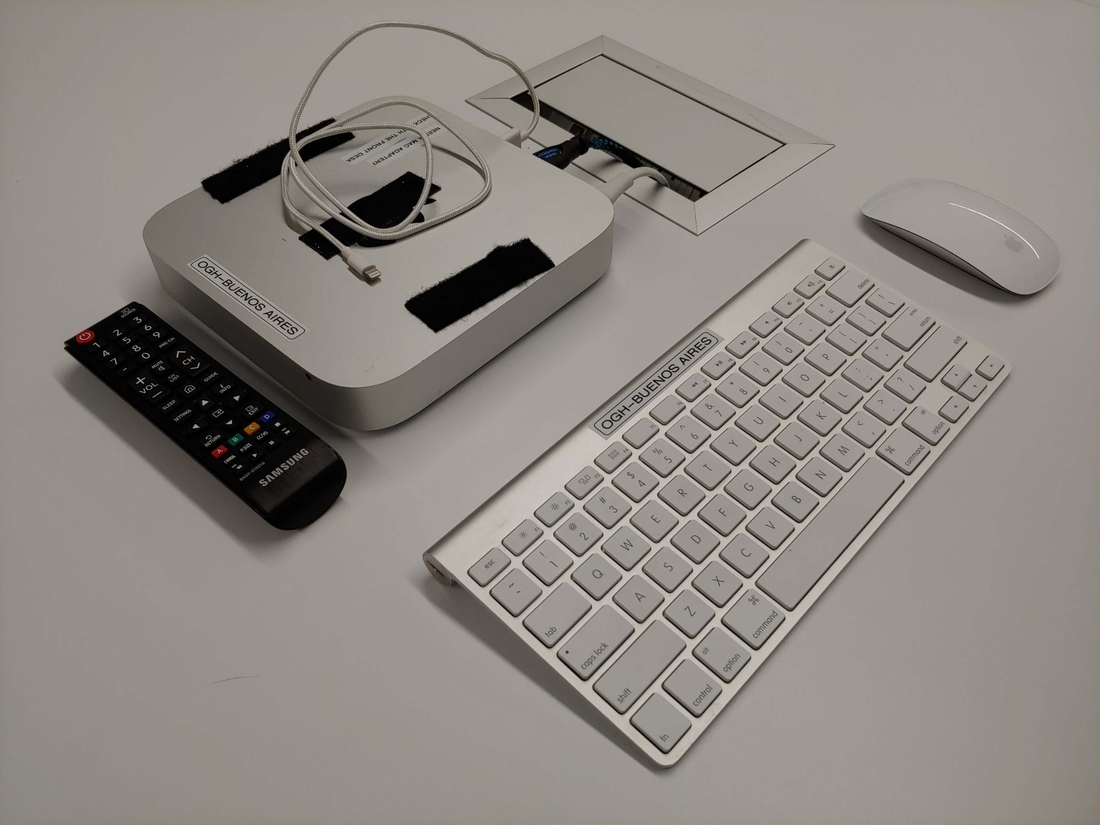 A silver desktop setup featuring a wireless keyboard, a computer mouse, a remote control, and a docking station with visible cables.