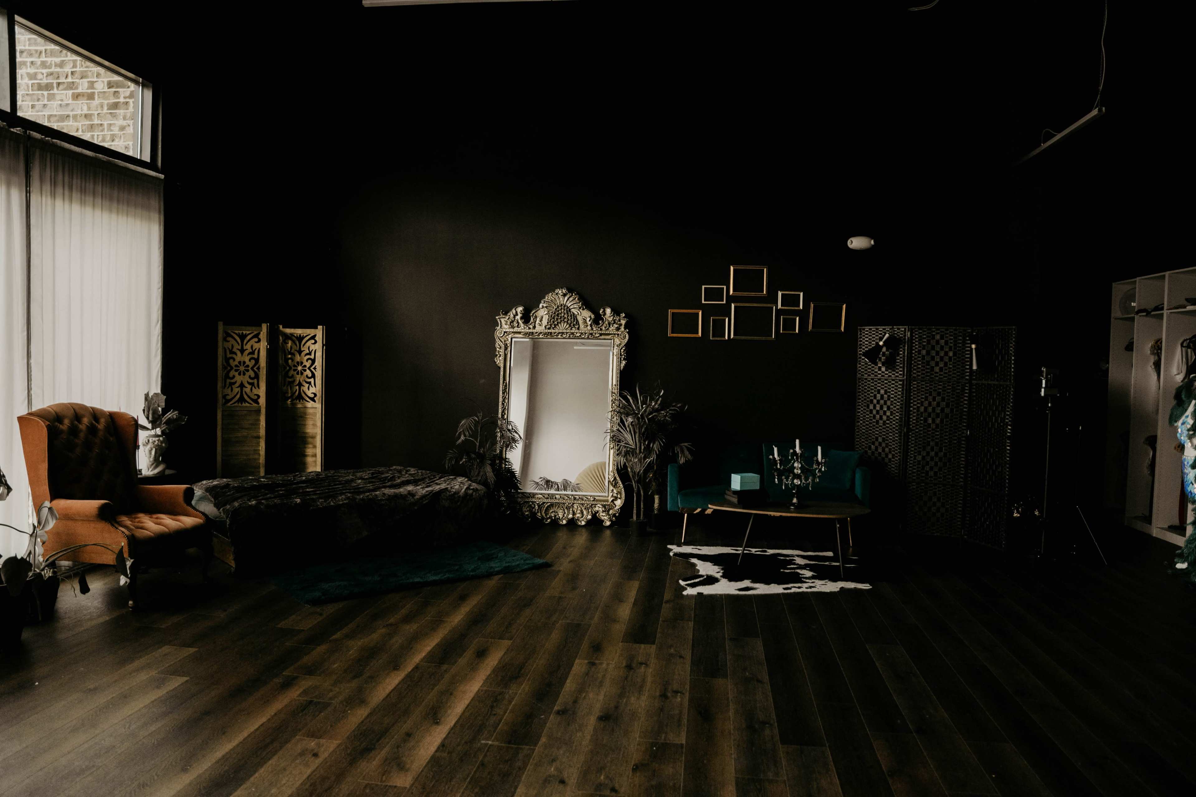 The image depicts a stylish interior space featuring a large ornate mirror, a velvet couch, a coffee table, and decorative elements against a dark wall.