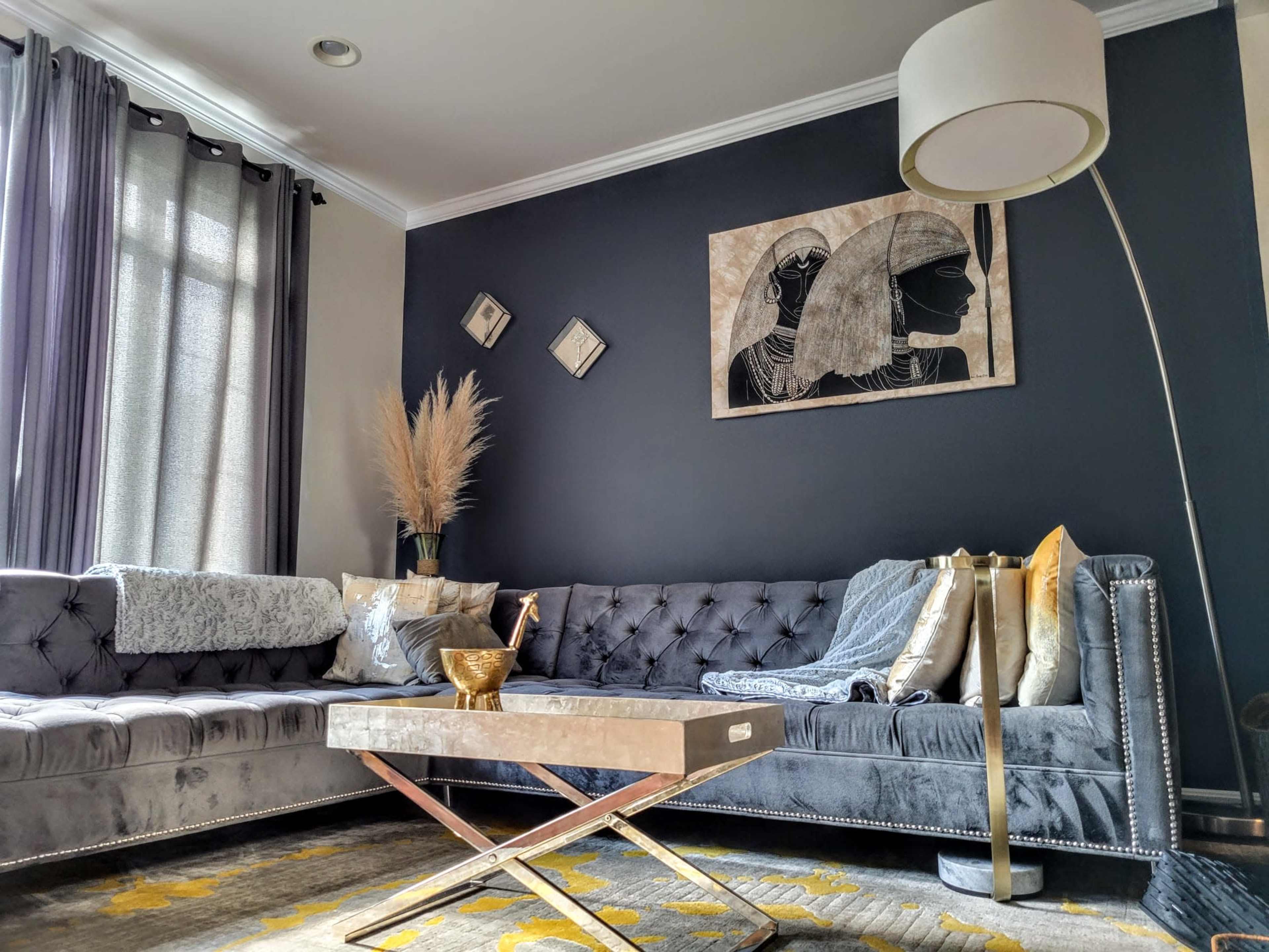A modern living room with a gray sectional sofa, decorative pillows, a coffee table, and a floor lamp against a dark wall featuring framed artwork.