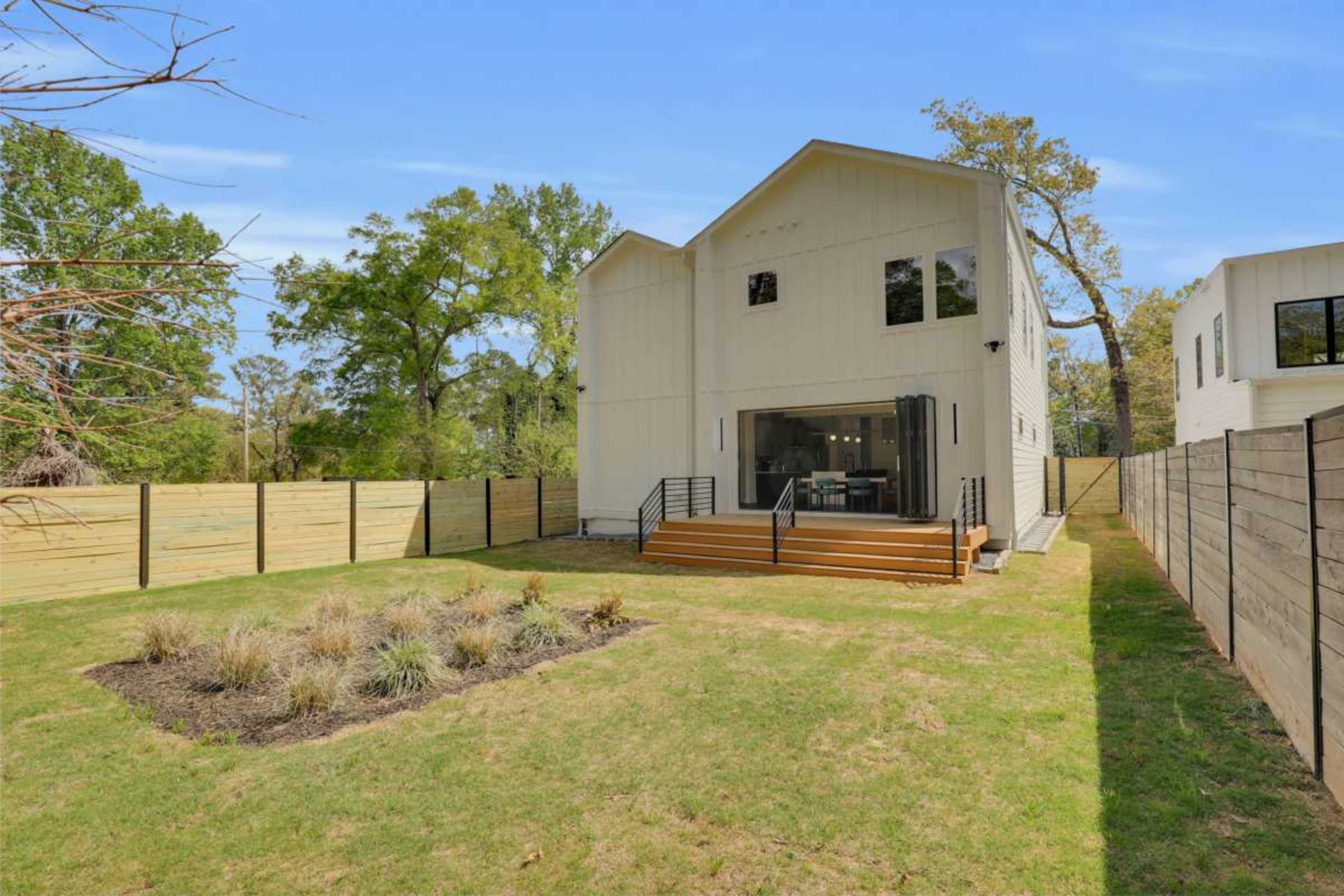 The image depicts a modern two-story house with large windows surrounded by a manicured lawn and wooden fences on either side.