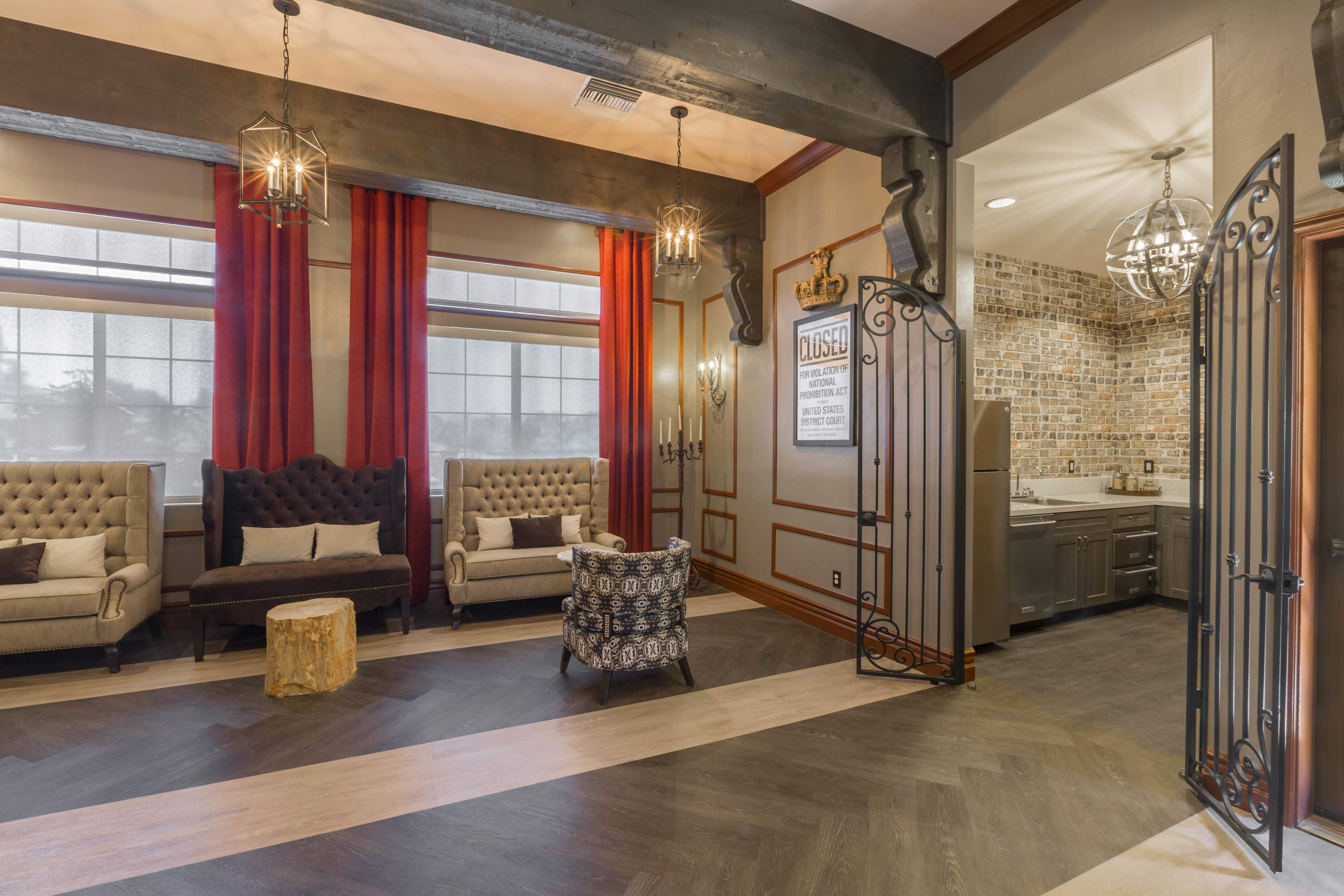 The image shows a modern interior space with two tufted chairs, a small wooden stump table, and a kitchenette visible through an ornate gate.