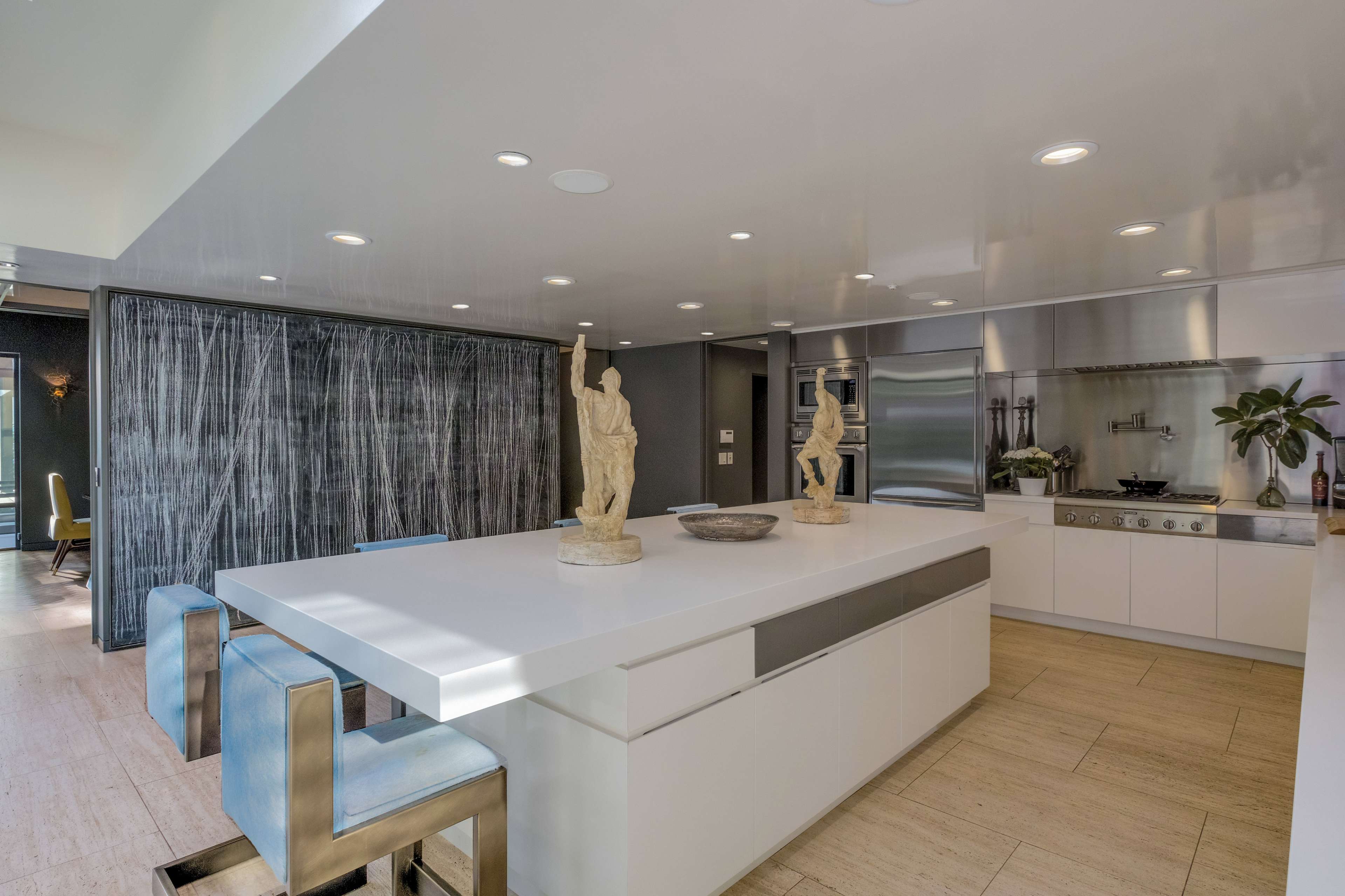 A modern kitchen features a large white island, stainless steel appliances, and decorative statues on the counter.