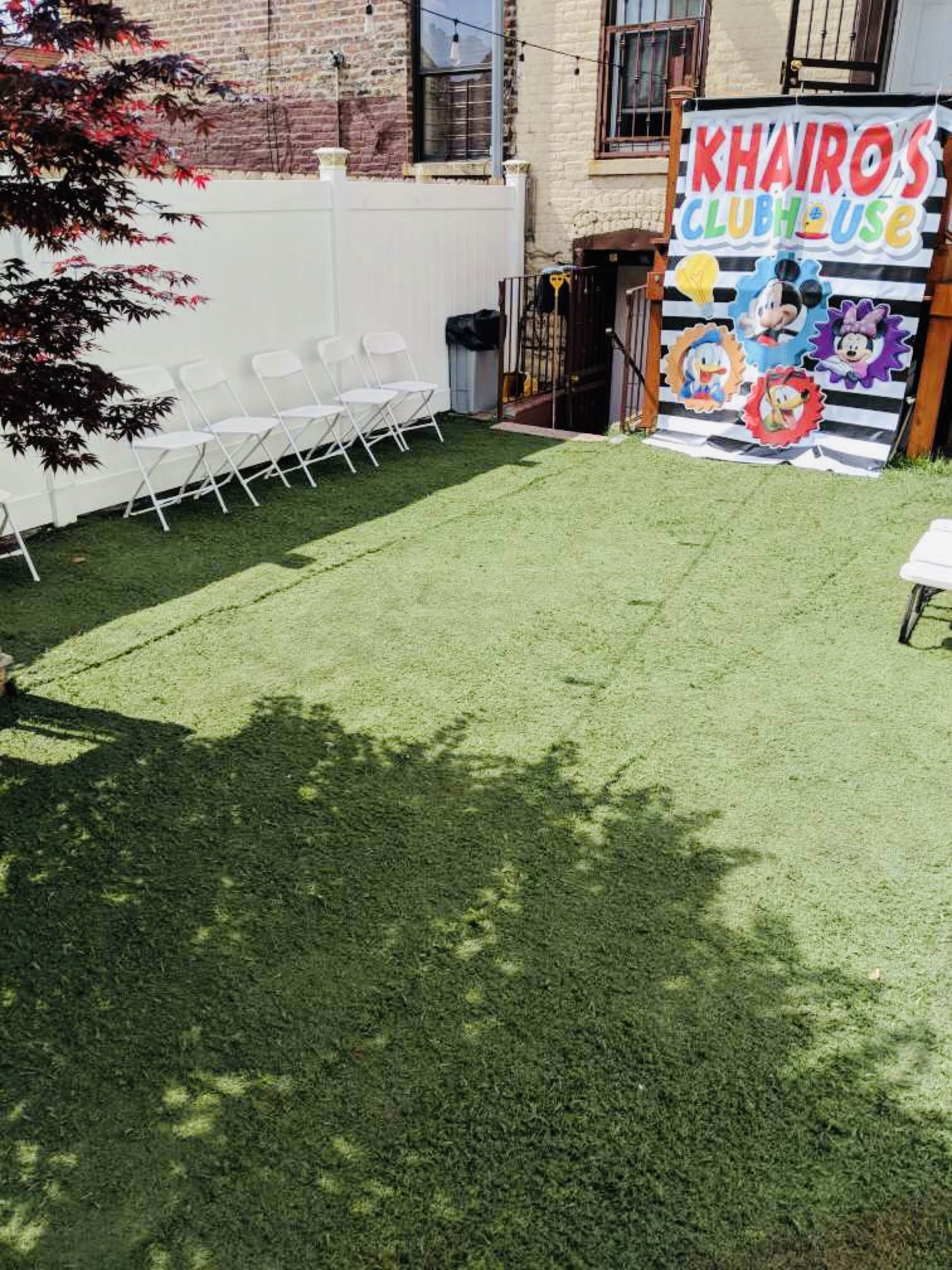 A grassy outdoor area set up for an event, featuring a backdrop with colorful cartoon characters and rows of white folding chairs.