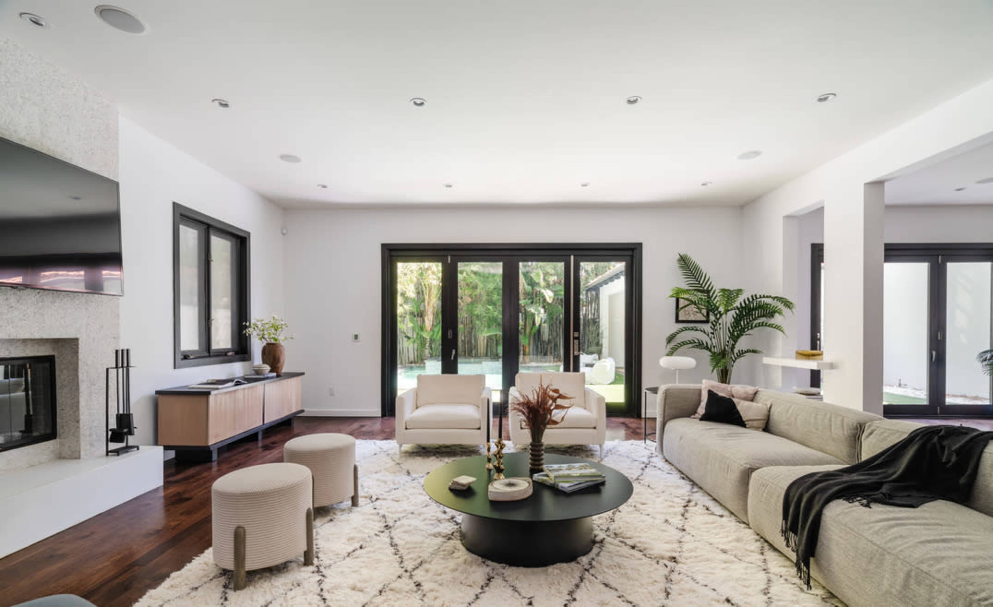 A modern living room with a sectional sofa, a round coffee table, and large windows overlooking a backyard with greenery.