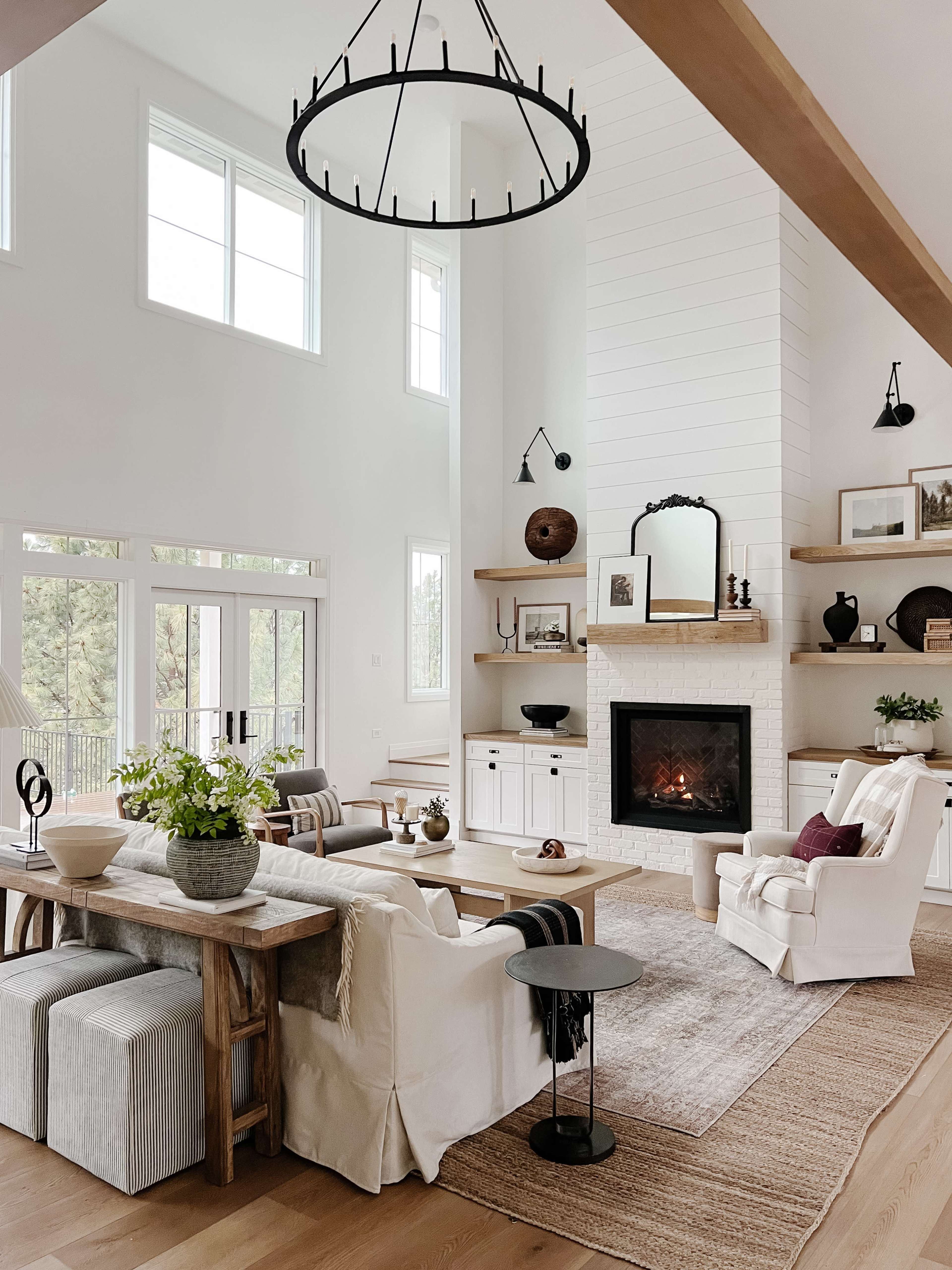 The image shows a bright, modern living room with high ceilings, a fireplace, and a mix of furniture including a dining table and comfortable seating.