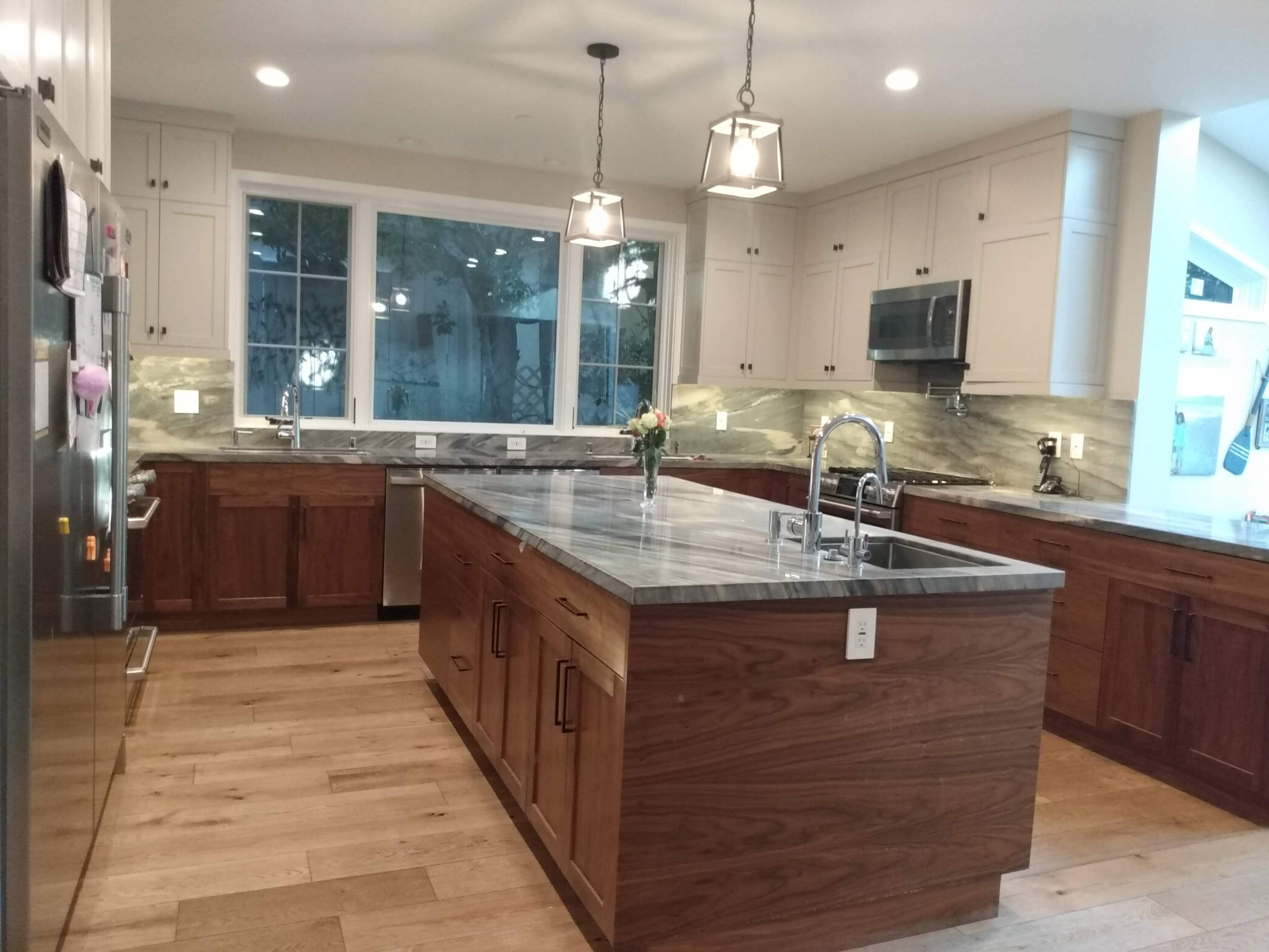 A modern kitchen featuring wooden cabinets, a large island with a marbled countertop, and stainless steel appliances.