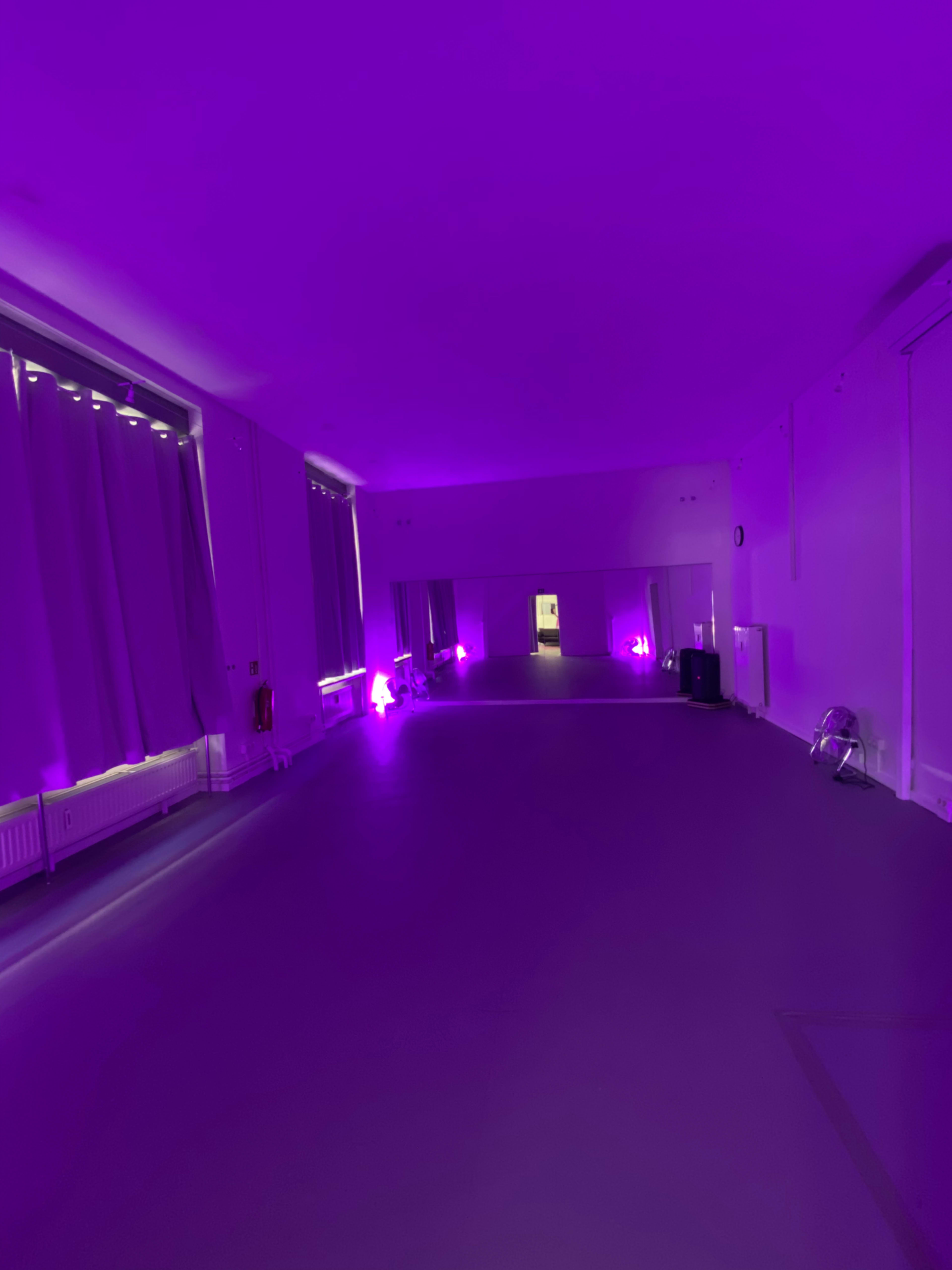 A dimly lit room with purple lighting, featuring curtains, mirrors, and a smooth floor.