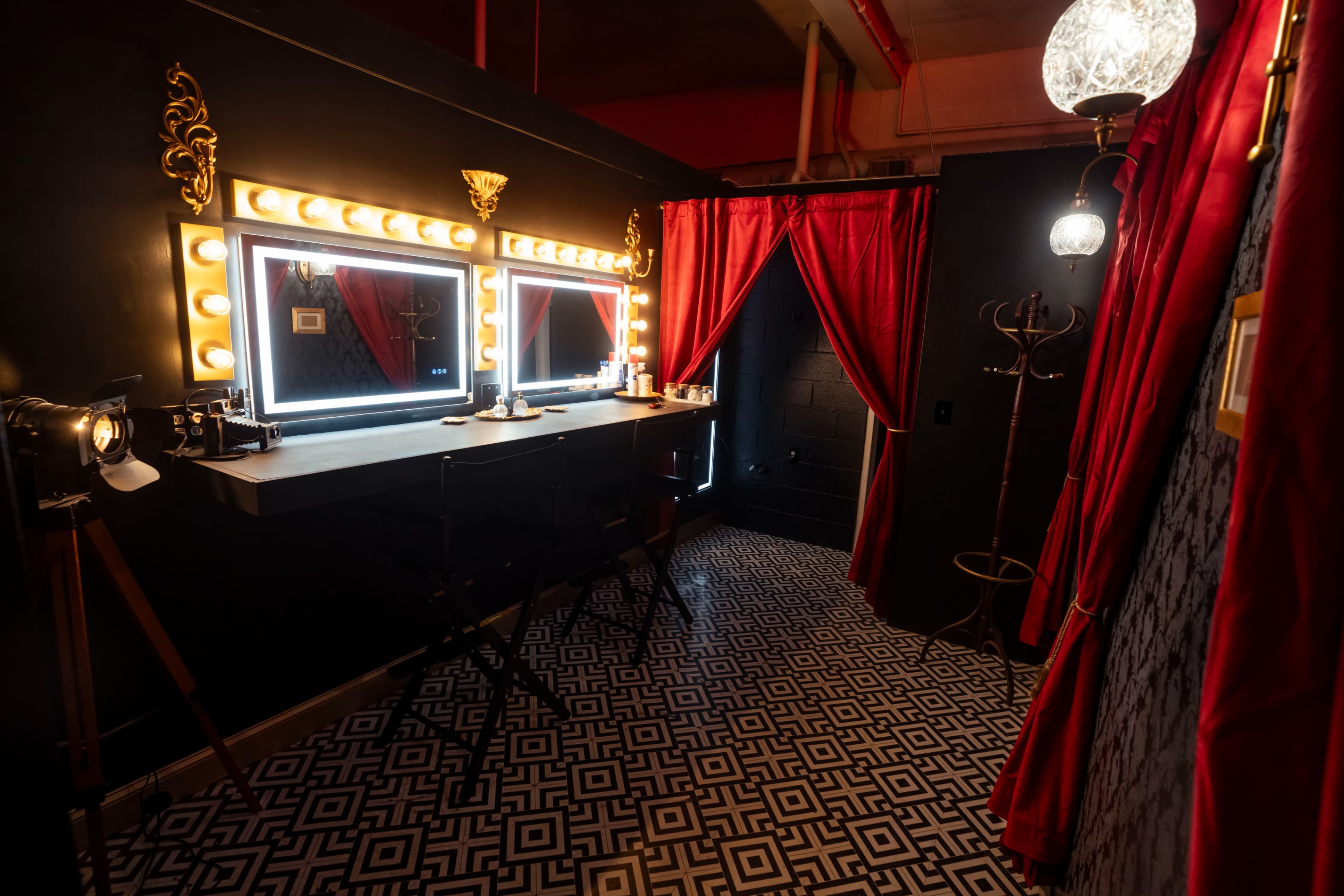 A well-equipped vanity area with bright mirrors, red curtains, a patterned floor, and elegant lighting fixtures.
