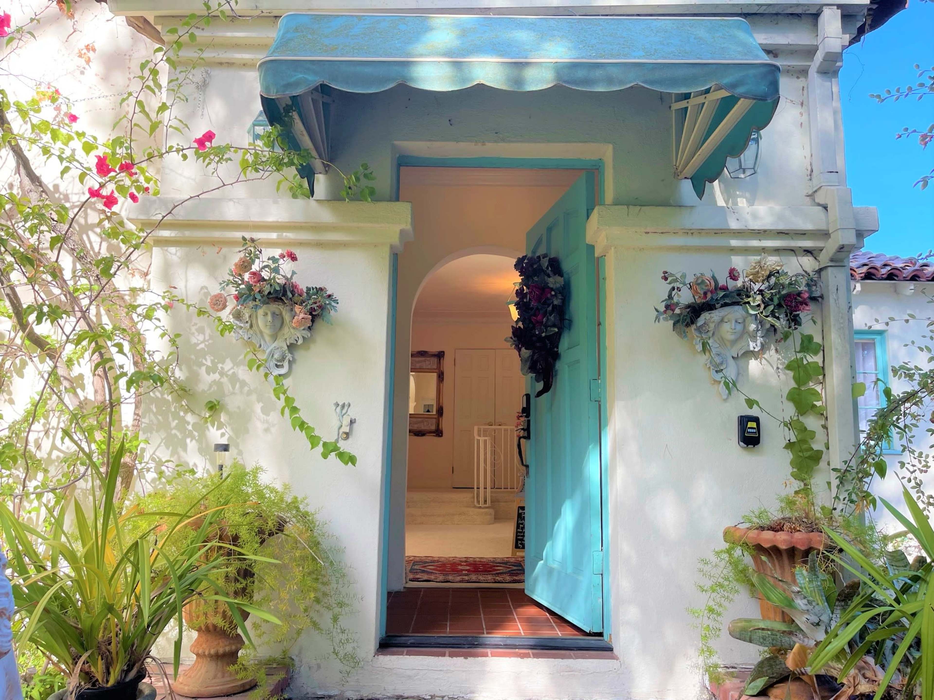An inviting entrance with a light blue door framed by potted plants and floral decorations on either side.