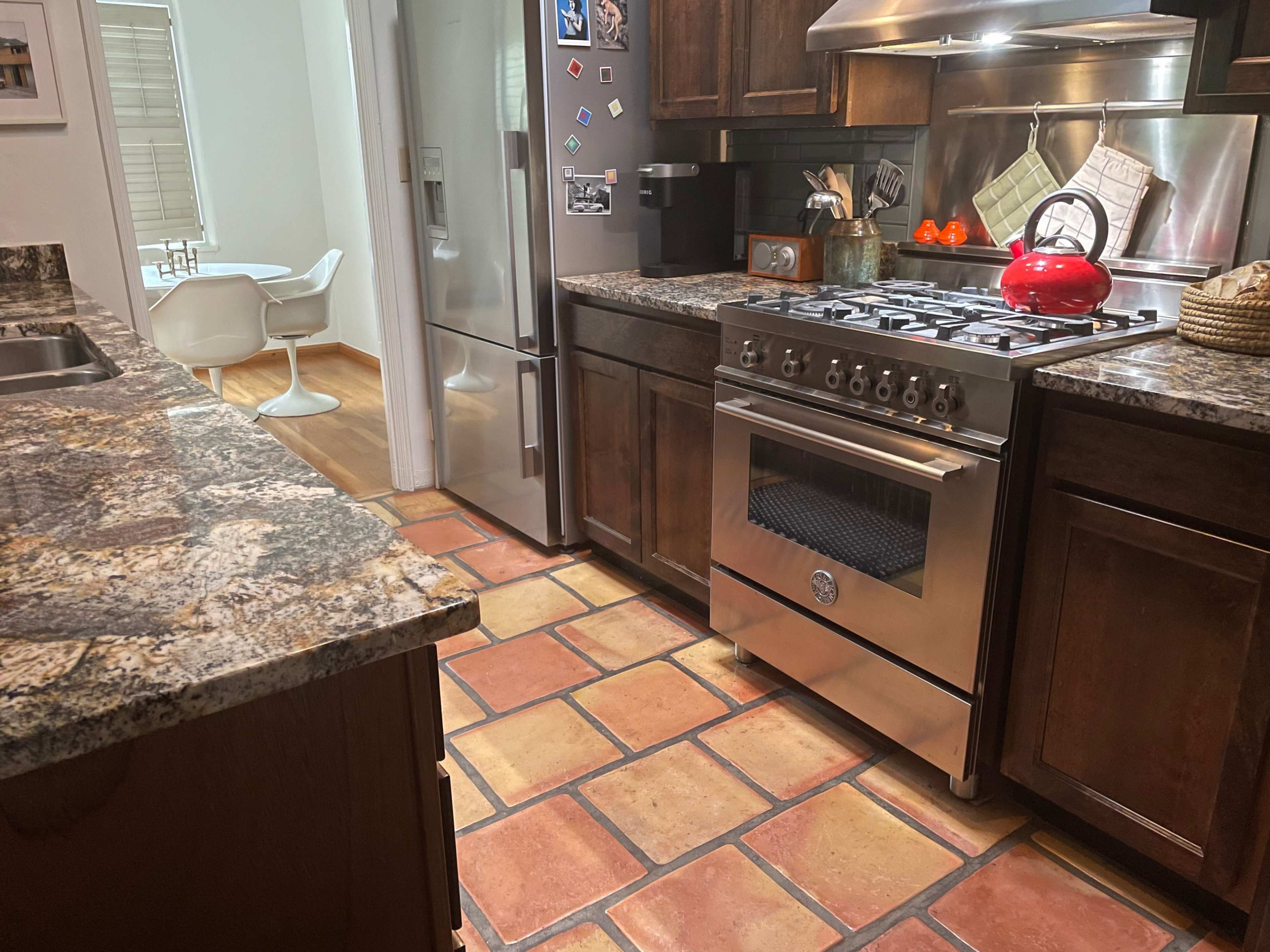 The kitchen features granite countertops, a stainless steel stove, a red kettle on the stove, and tiled flooring.