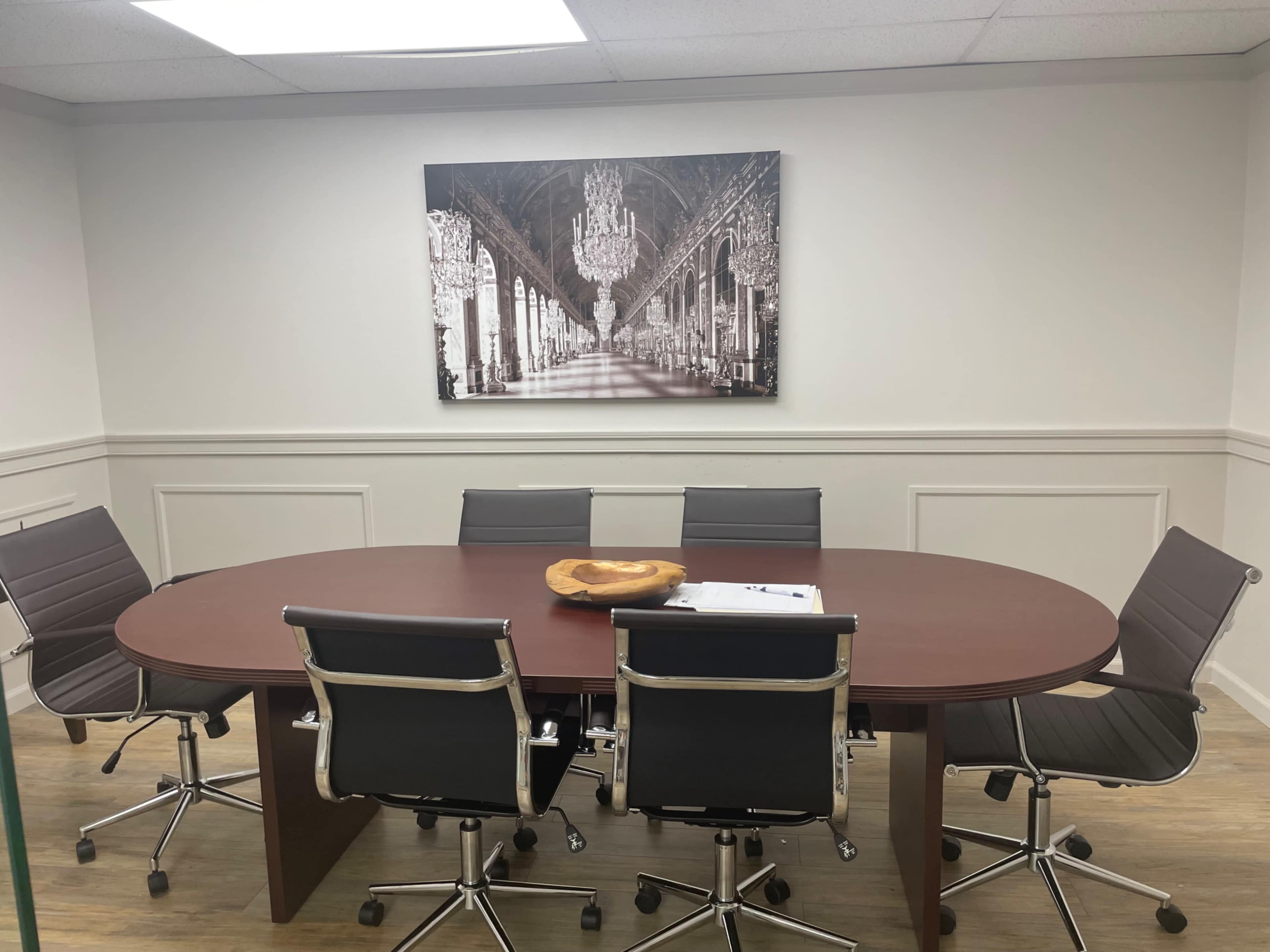 A modern conference room with an oval table surrounded by six black chairs and a large framed black-and-white photograph on the wall.