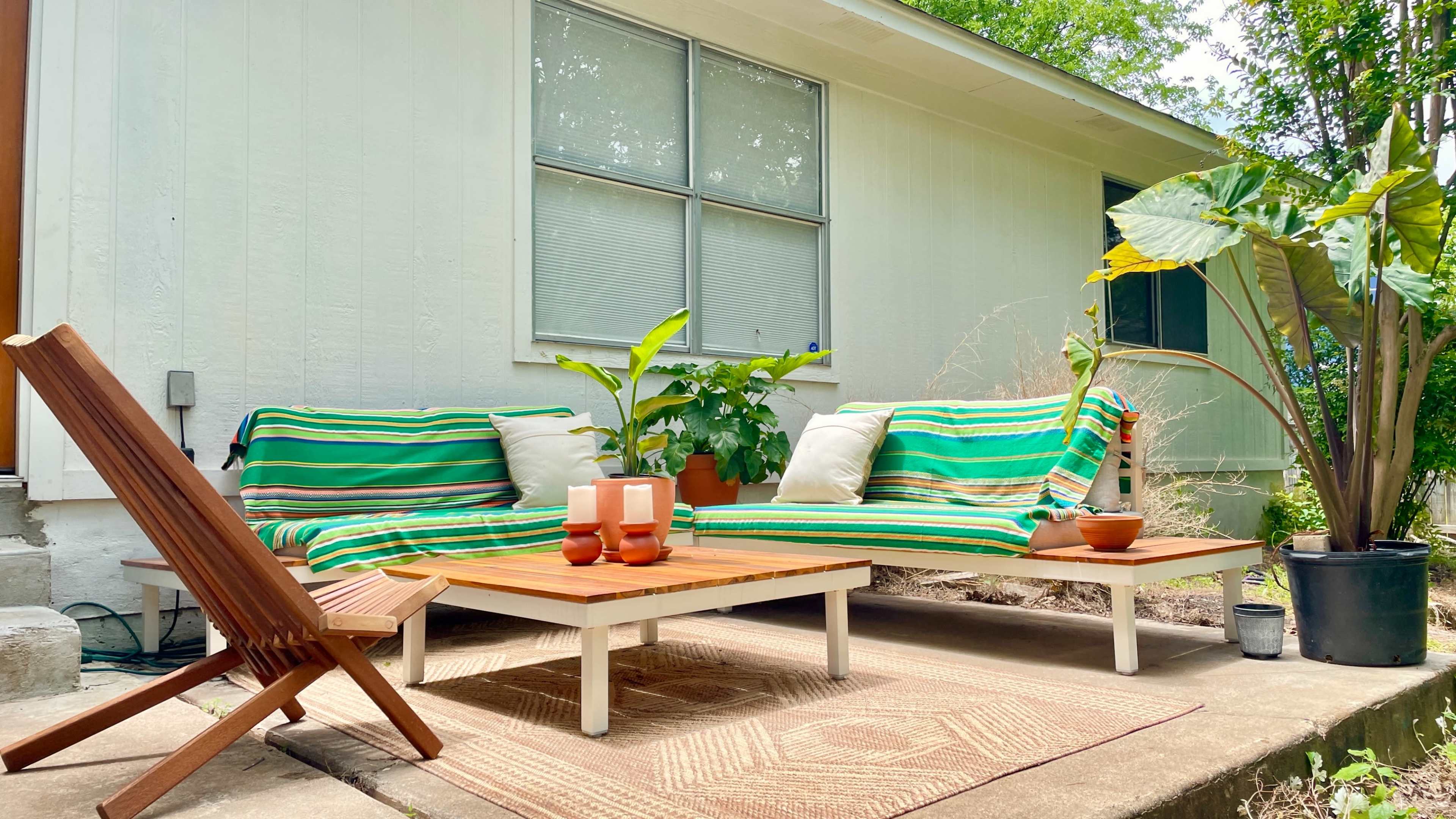 A seating area featuring two couches with striped covers, a coffee table, and a wooden chair on a concrete patio beside a house.