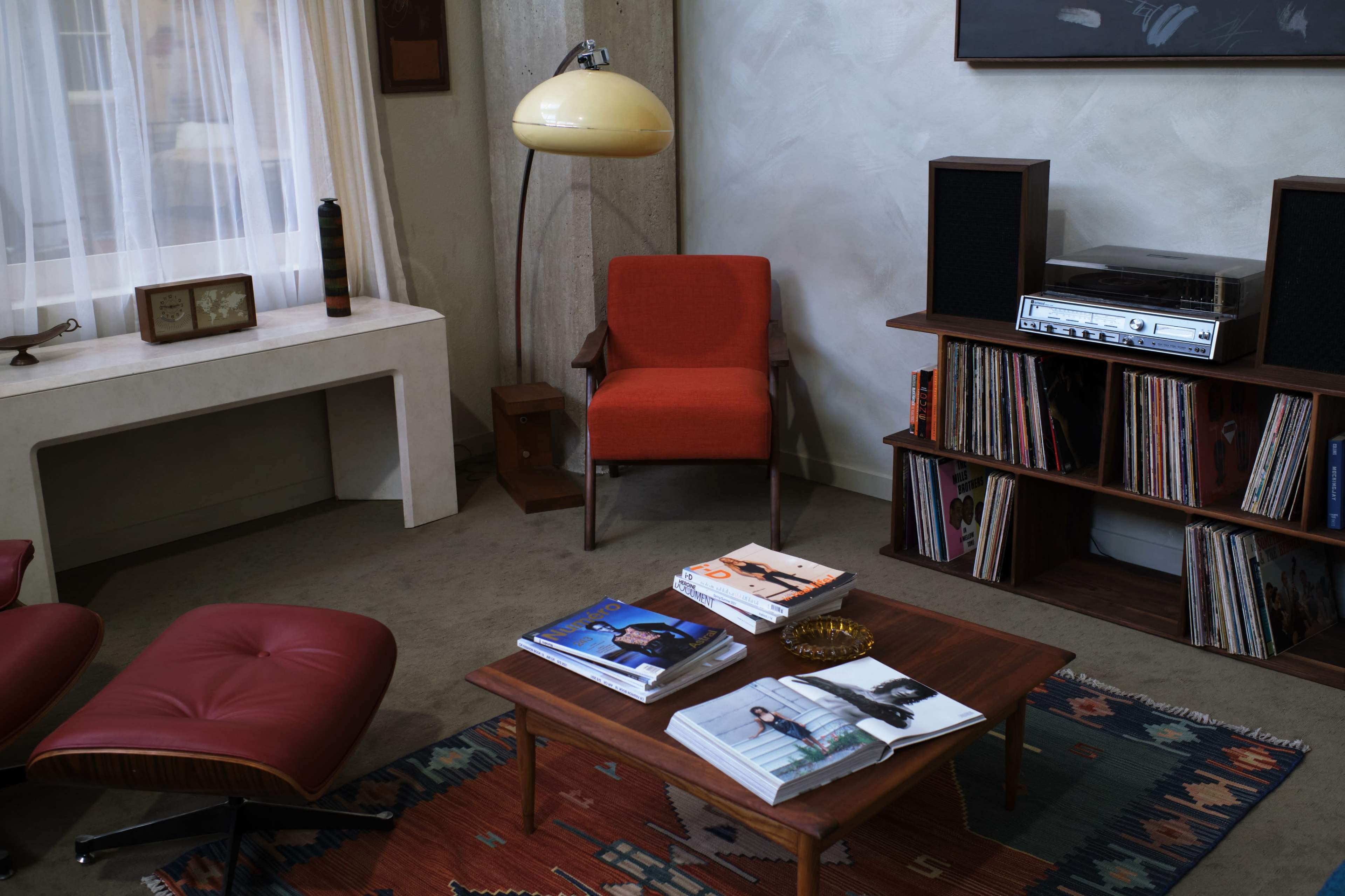 A mid-century modern living room featuring an orange chair, a record player with vinyl records, and a patterned rug.
