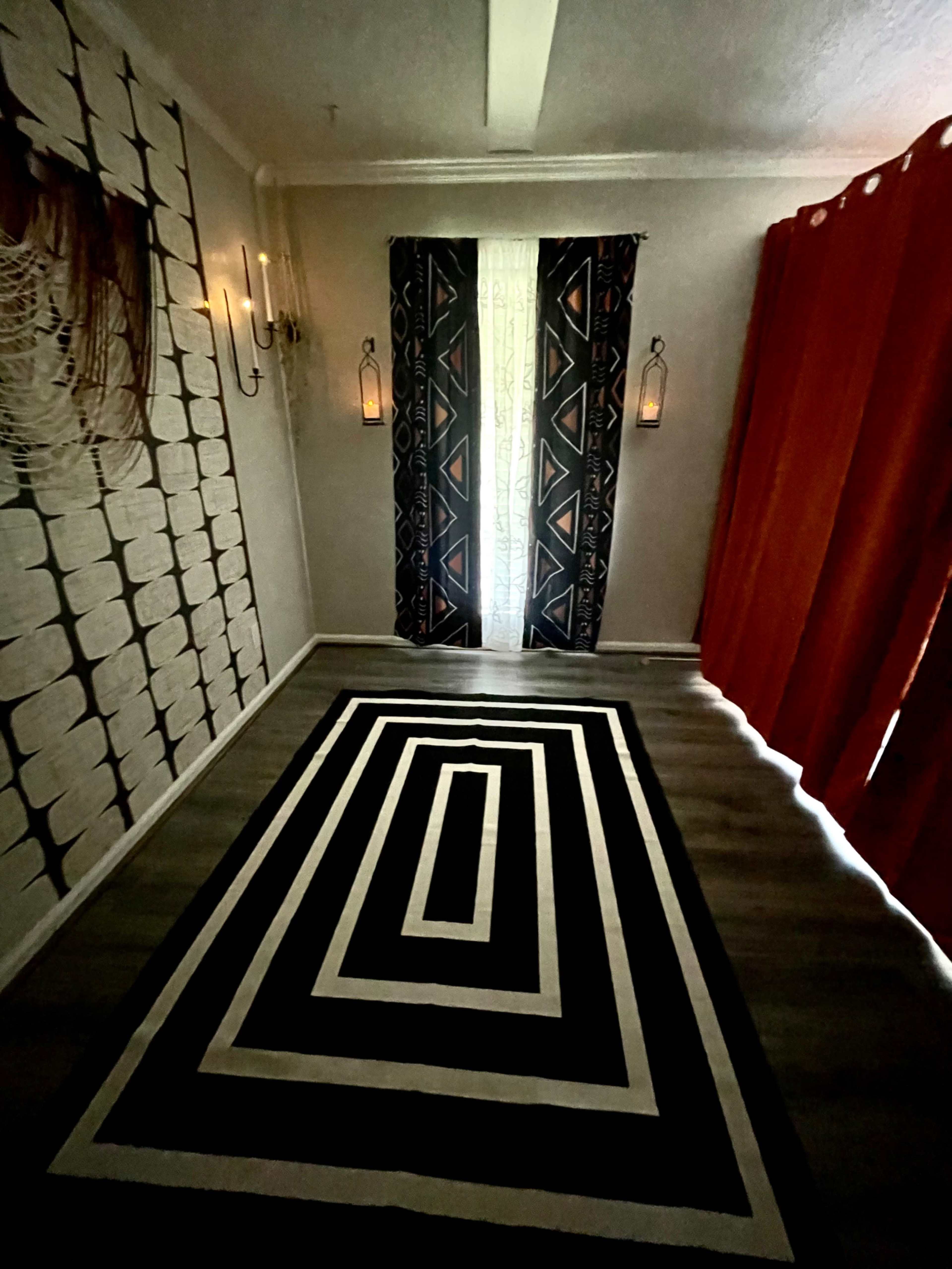 The room features a striped black and white rug, patterned curtains, and wall sconces illuminated on a textured wall.