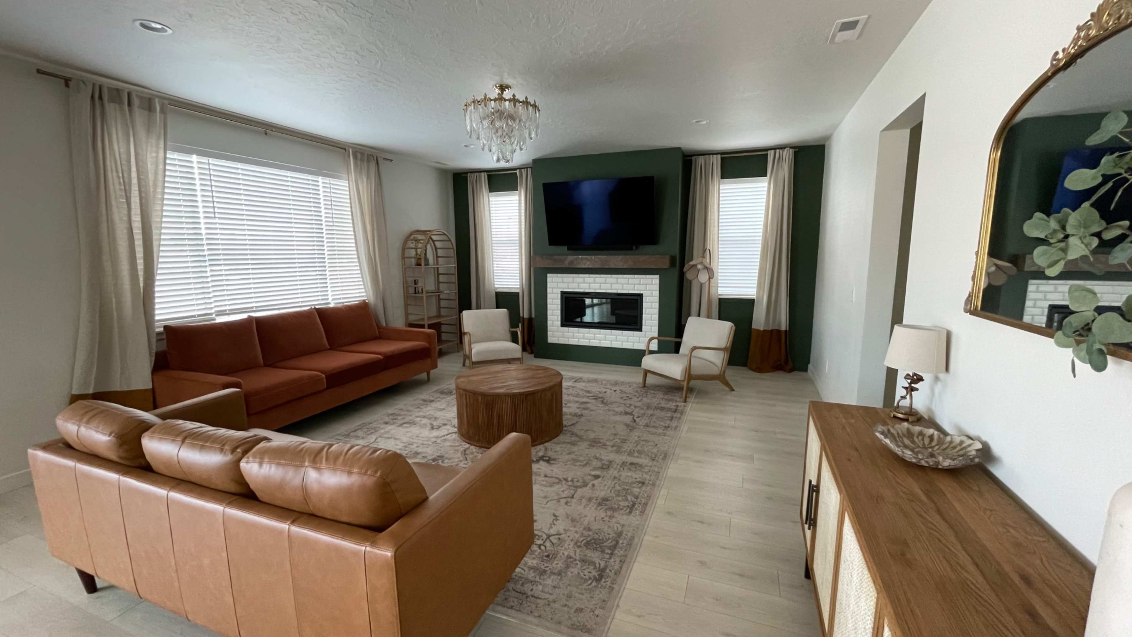 A modern living room features a brown leather sofa, a circular wooden coffee table, and a fireplace with a large television above it.