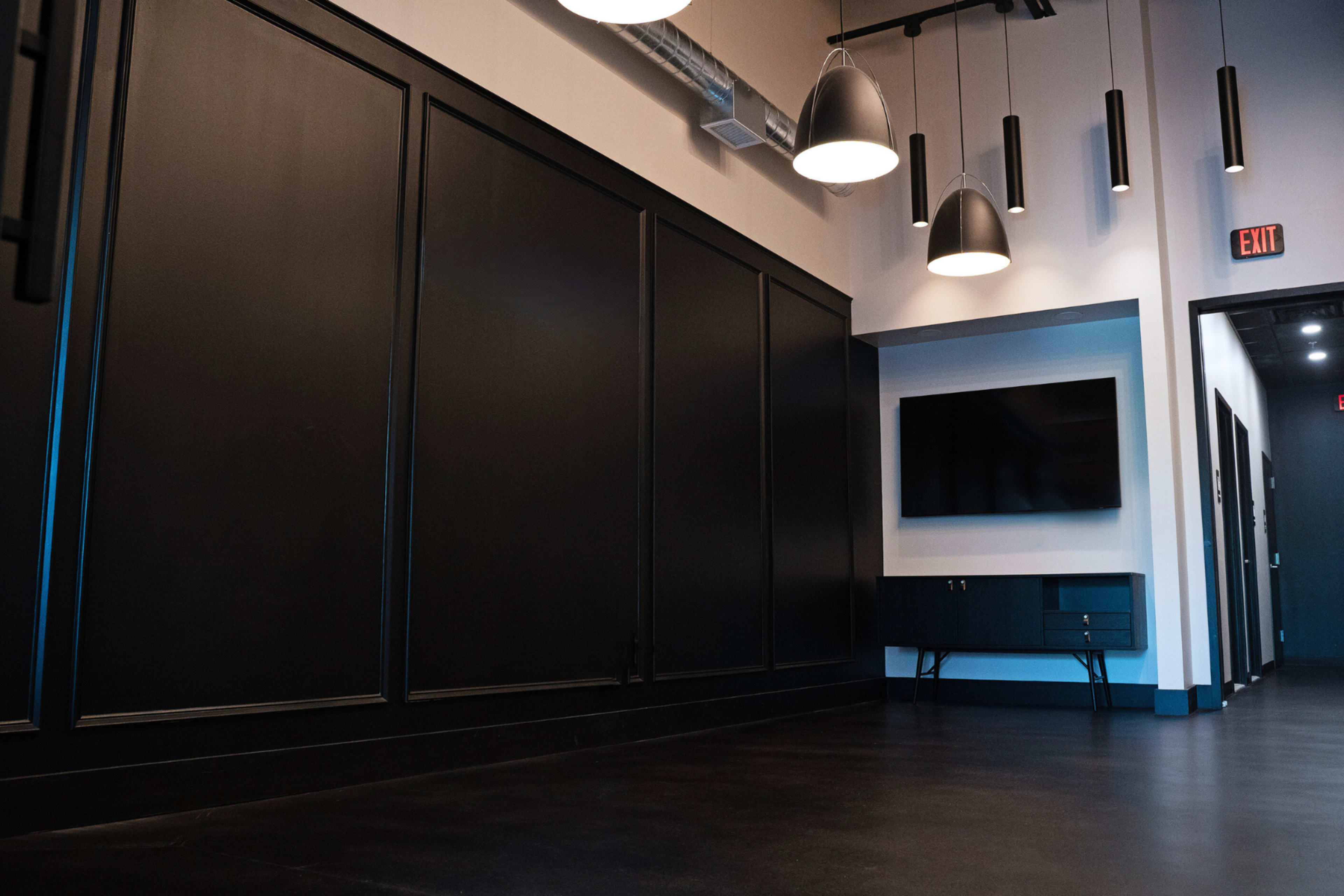 An interior space with black paneling, modern lighting fixtures hanging from the ceiling, and a wall-mounted television next to a console table.
