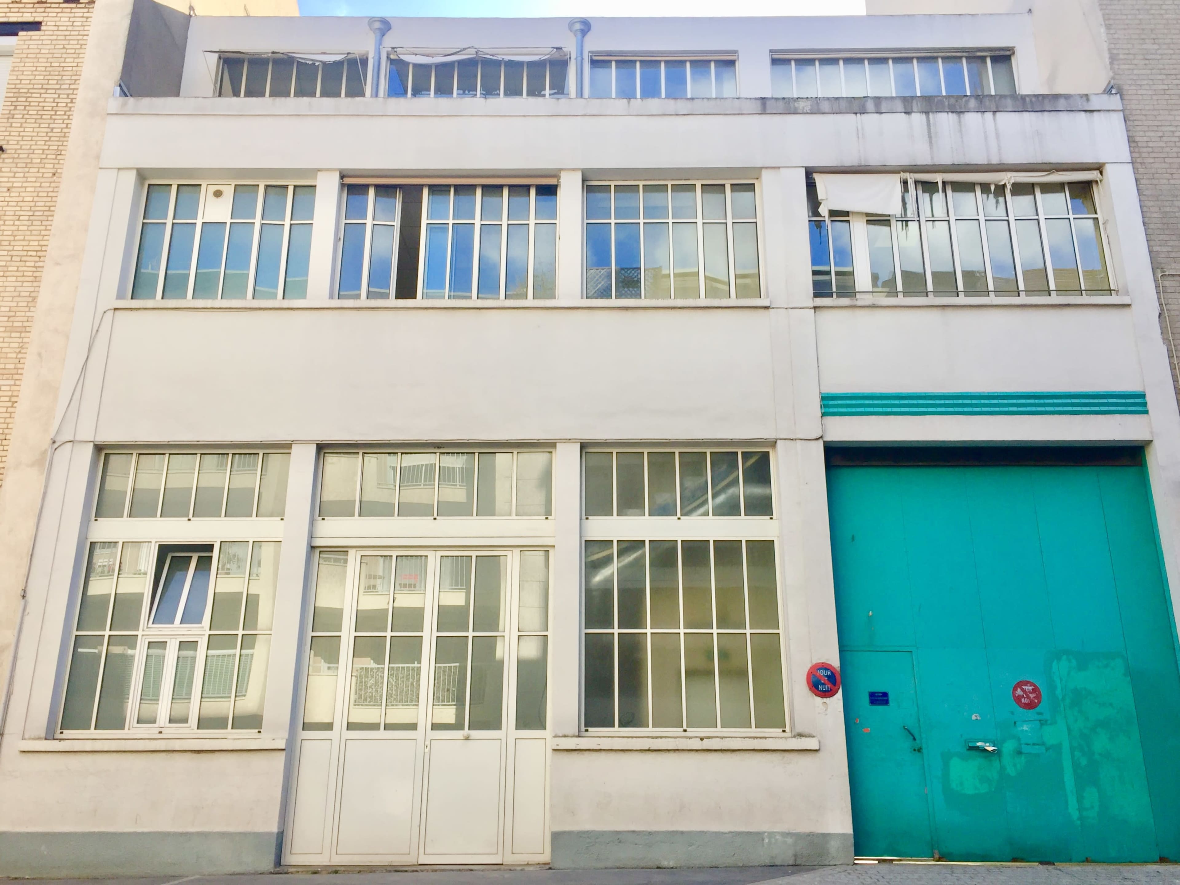 A modern building facade featuring large windows and a prominent turquoise door.