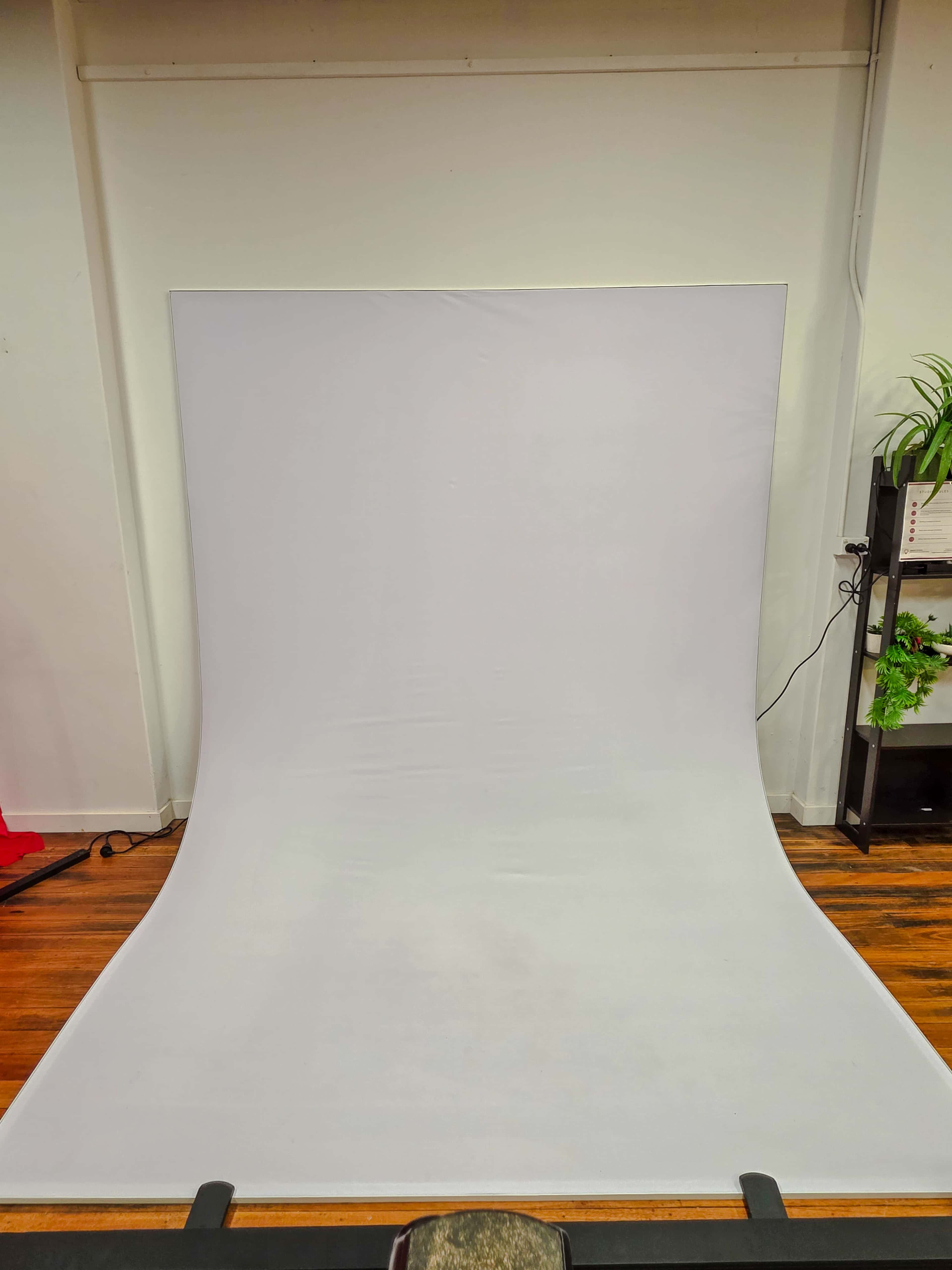 The image shows a plain white backdrop with a slight curve, set against a wall in a room with wooden flooring.