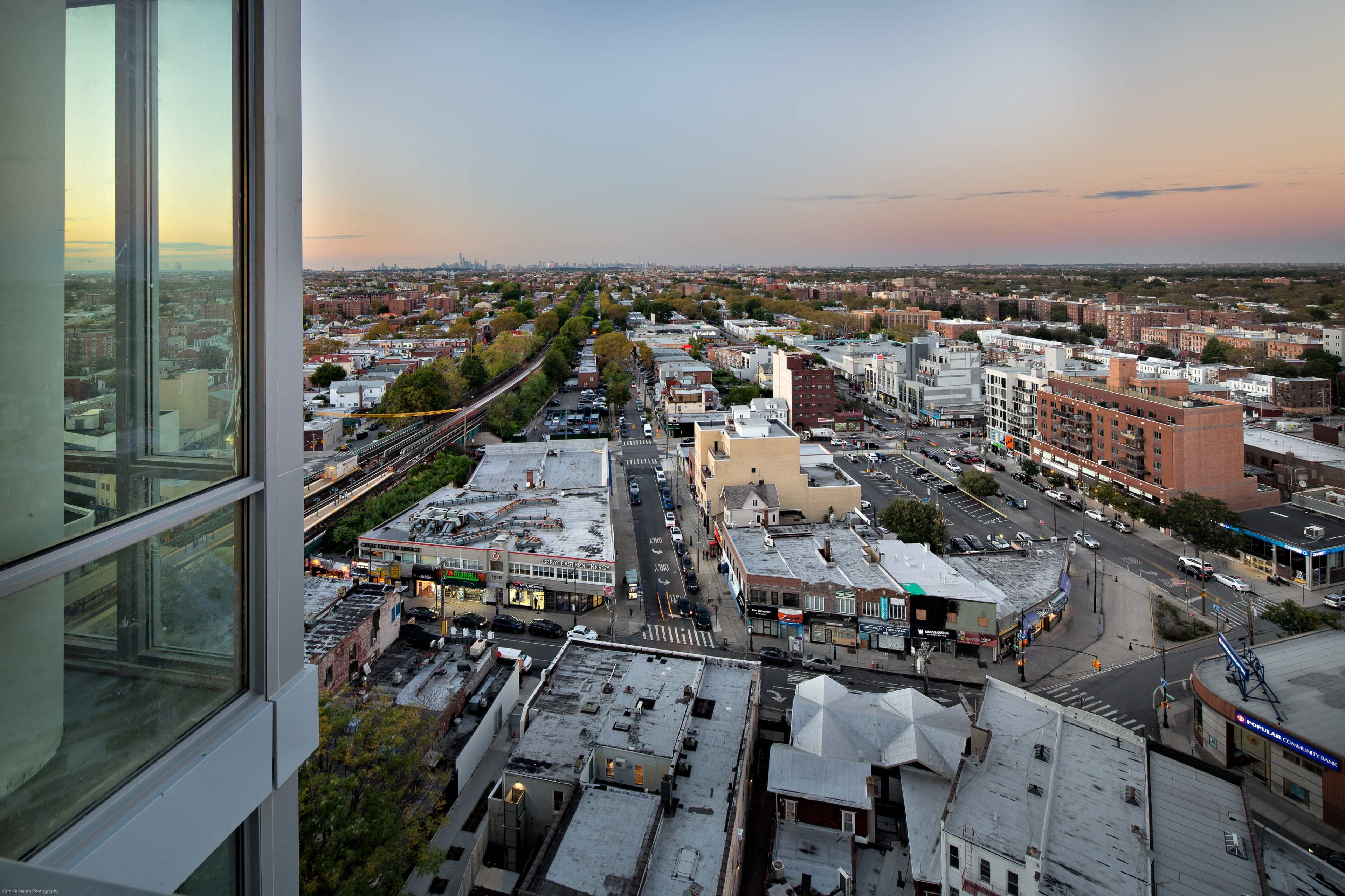 A view from a high building overlooking a cityscape with streets, buildings, and a distant skyline at sunset.