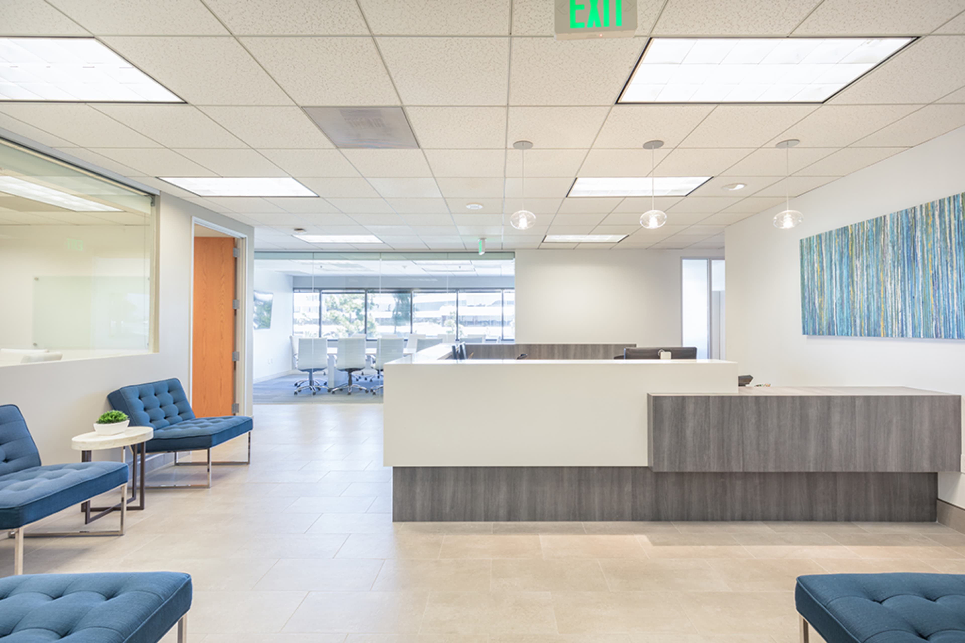 A modern office reception area with blue seating, a reception desk, and a conference room visible in the background.