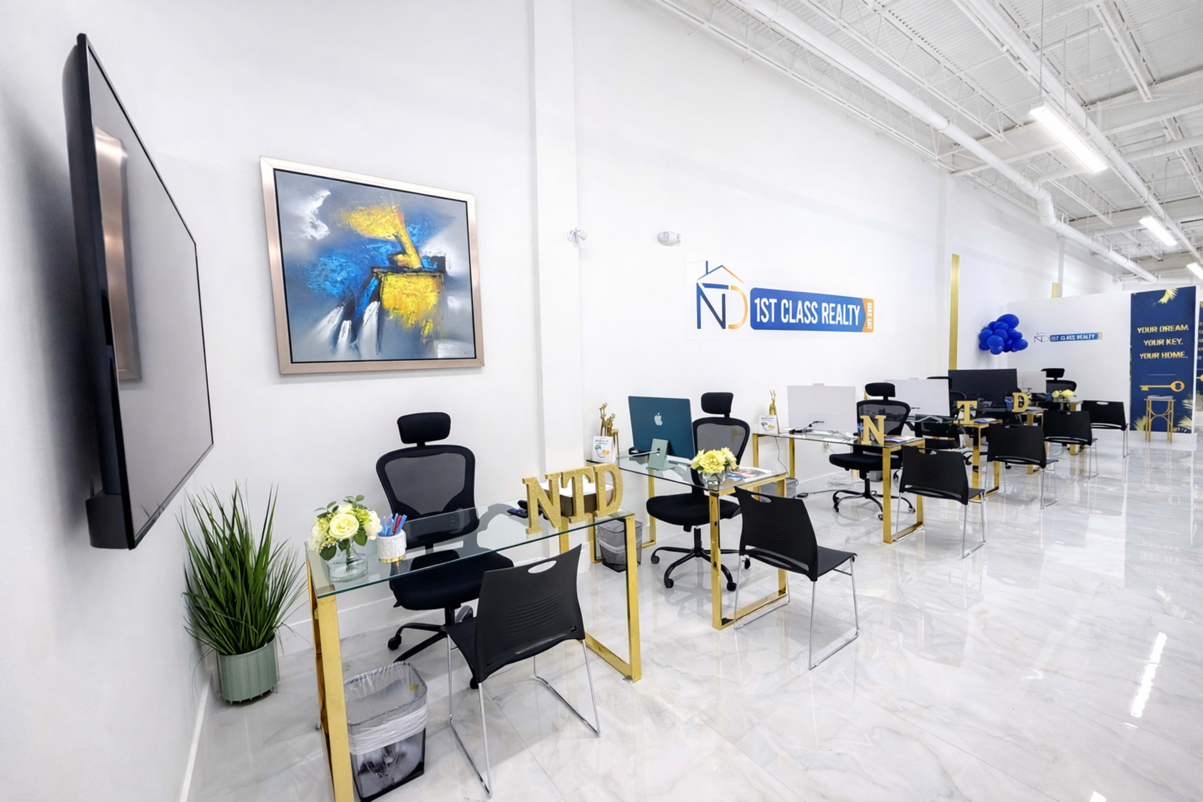 The image shows a modern office space with glass desks, ergonomic chairs, and decorative plants, featuring a prominent company logo on the wall.