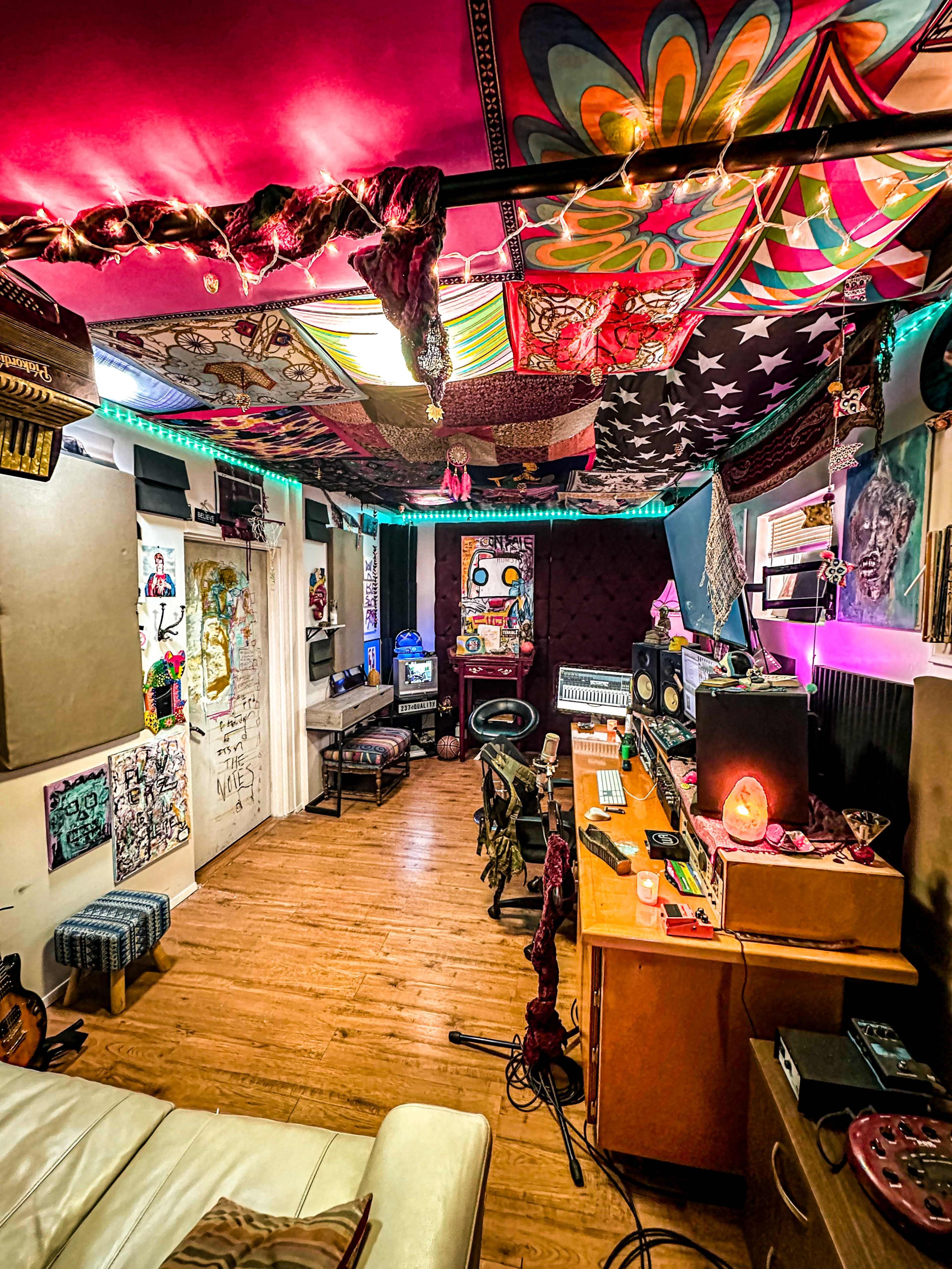 A vibrant music studio features colorful tapestries on the ceiling, illuminated by string lights, with various instruments and sound equipment arranged in the space.