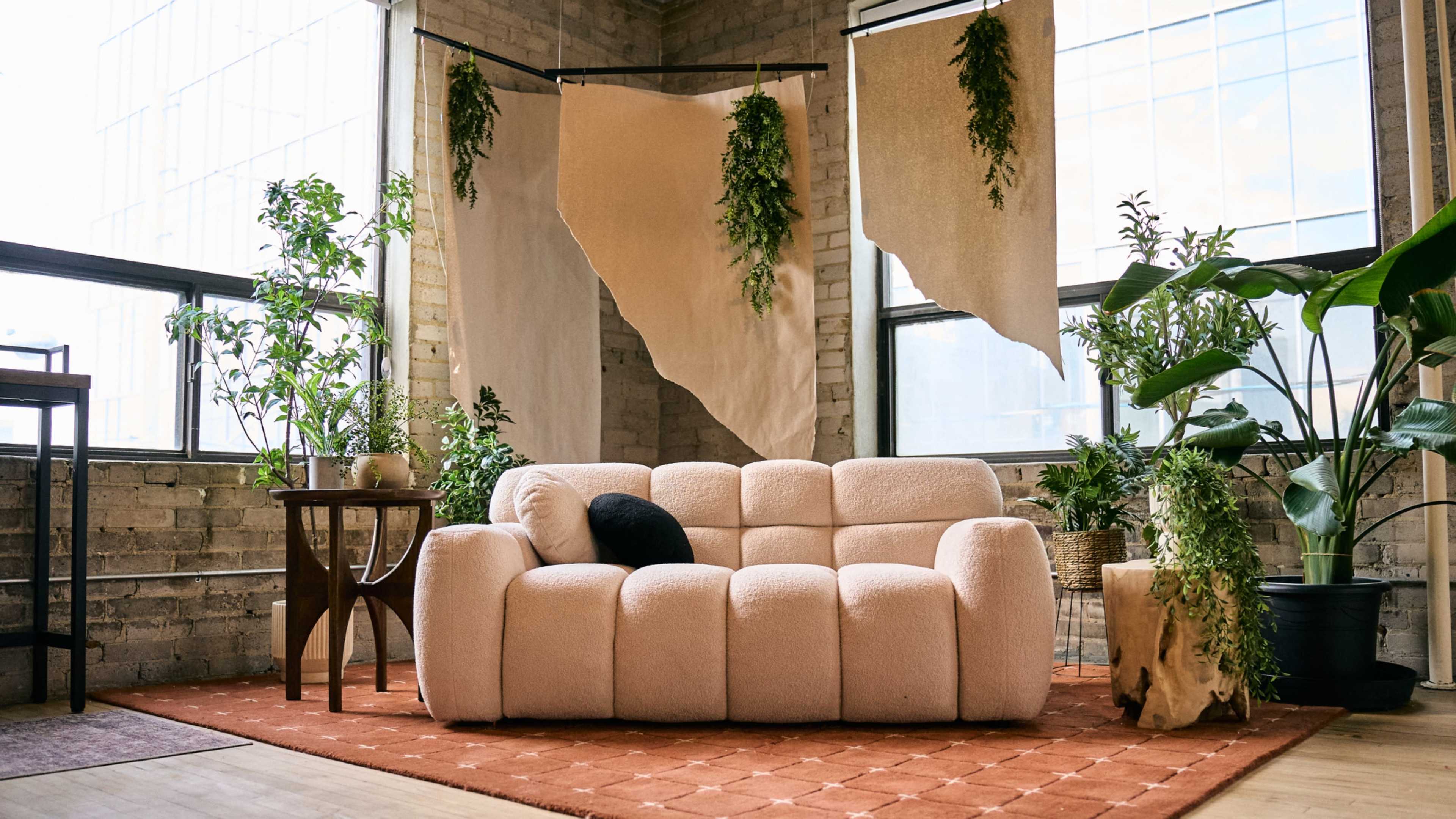 A light-colored, plush sofa is positioned in a room filled with various plants and decorated with fabric hangings.