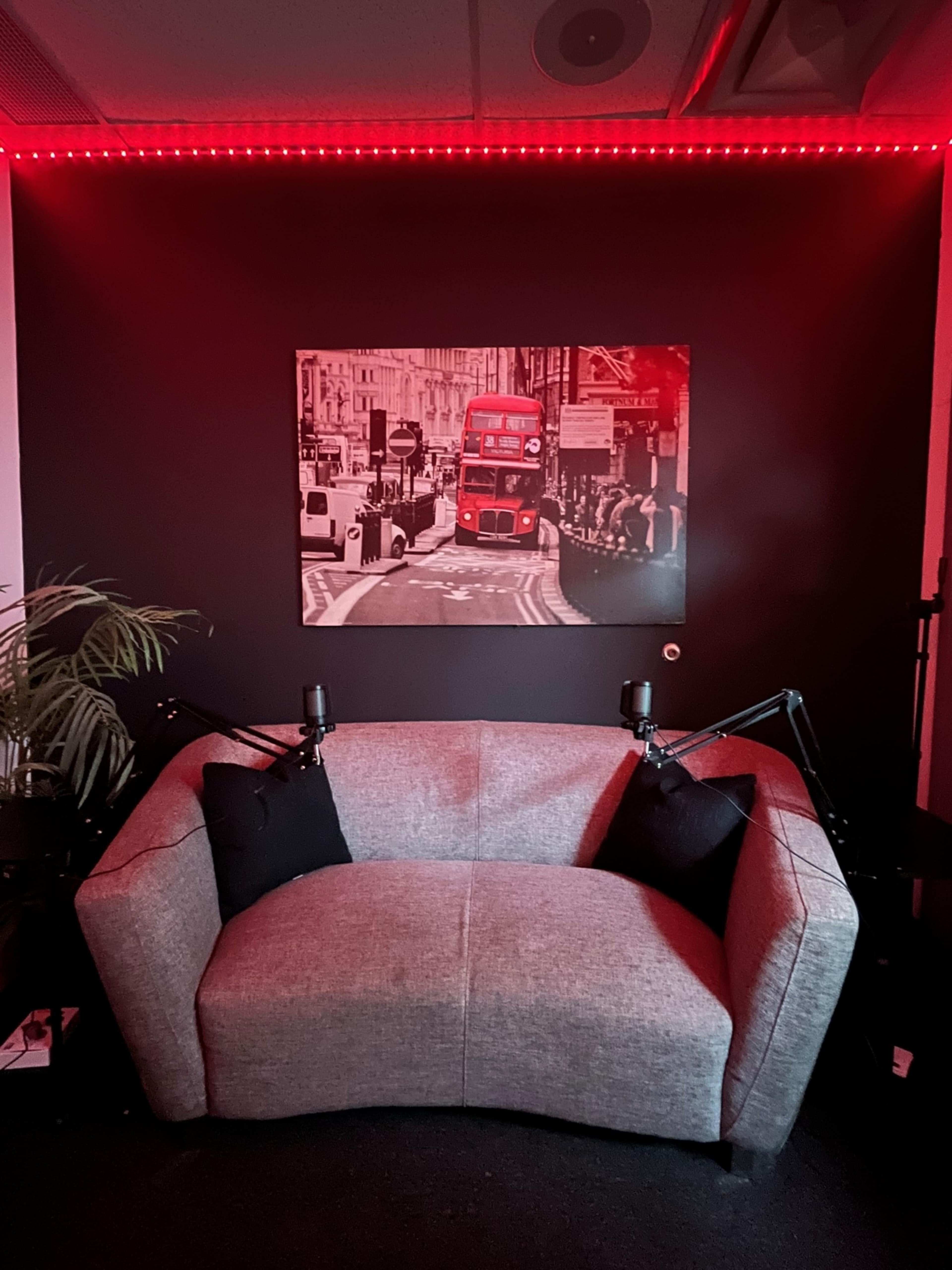 A gray sofa with black pillows is positioned in front of a black wall featuring a red-lit photograph of a London street scene.