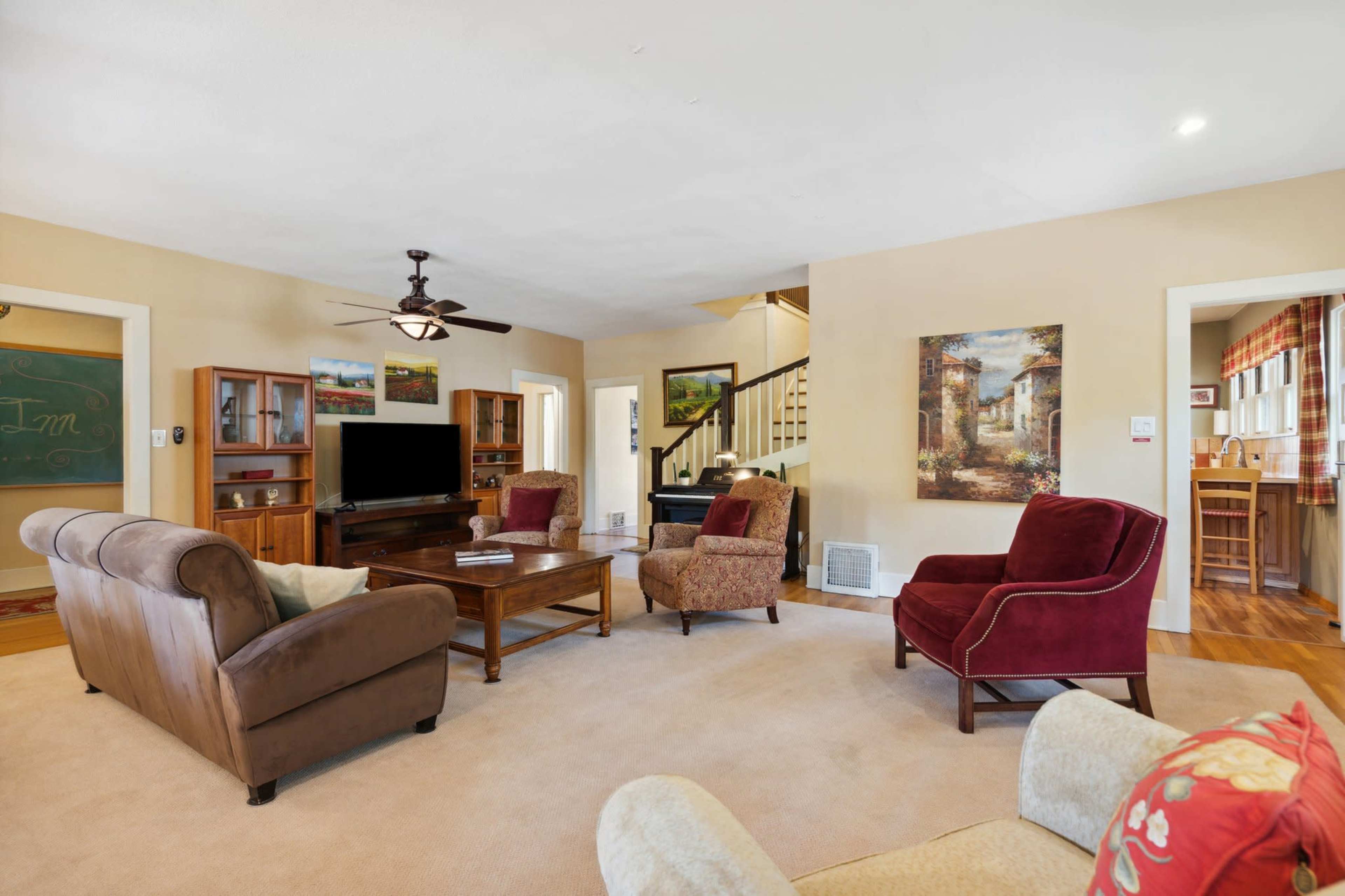 The living room features a cozy arrangement of brown and burgundy armchairs around a wooden coffee table, with a large TV cabinet and paintings on the walls.