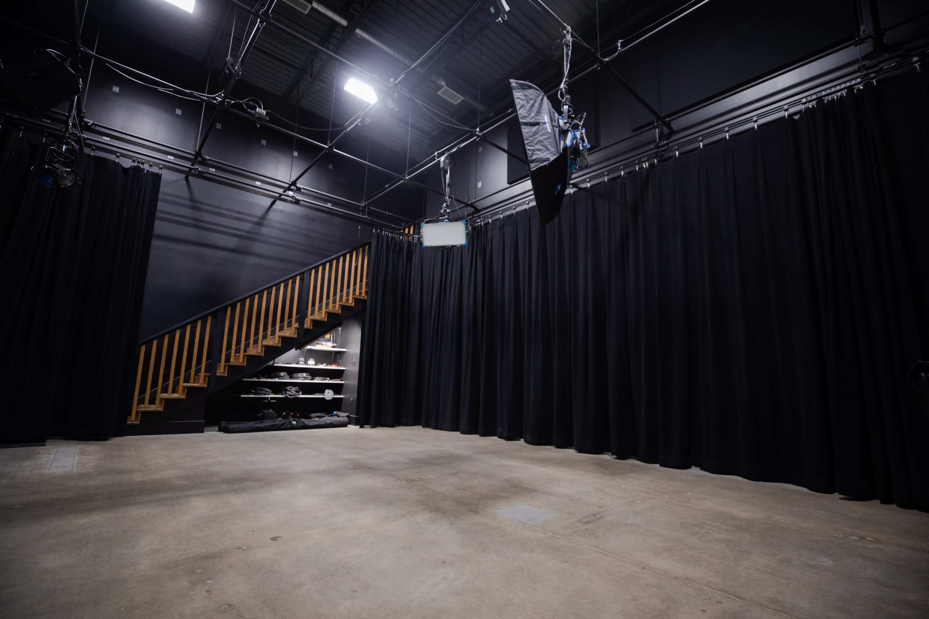 A dimly lit studio space with black curtains, a wooden staircase, and various items on a shelf.