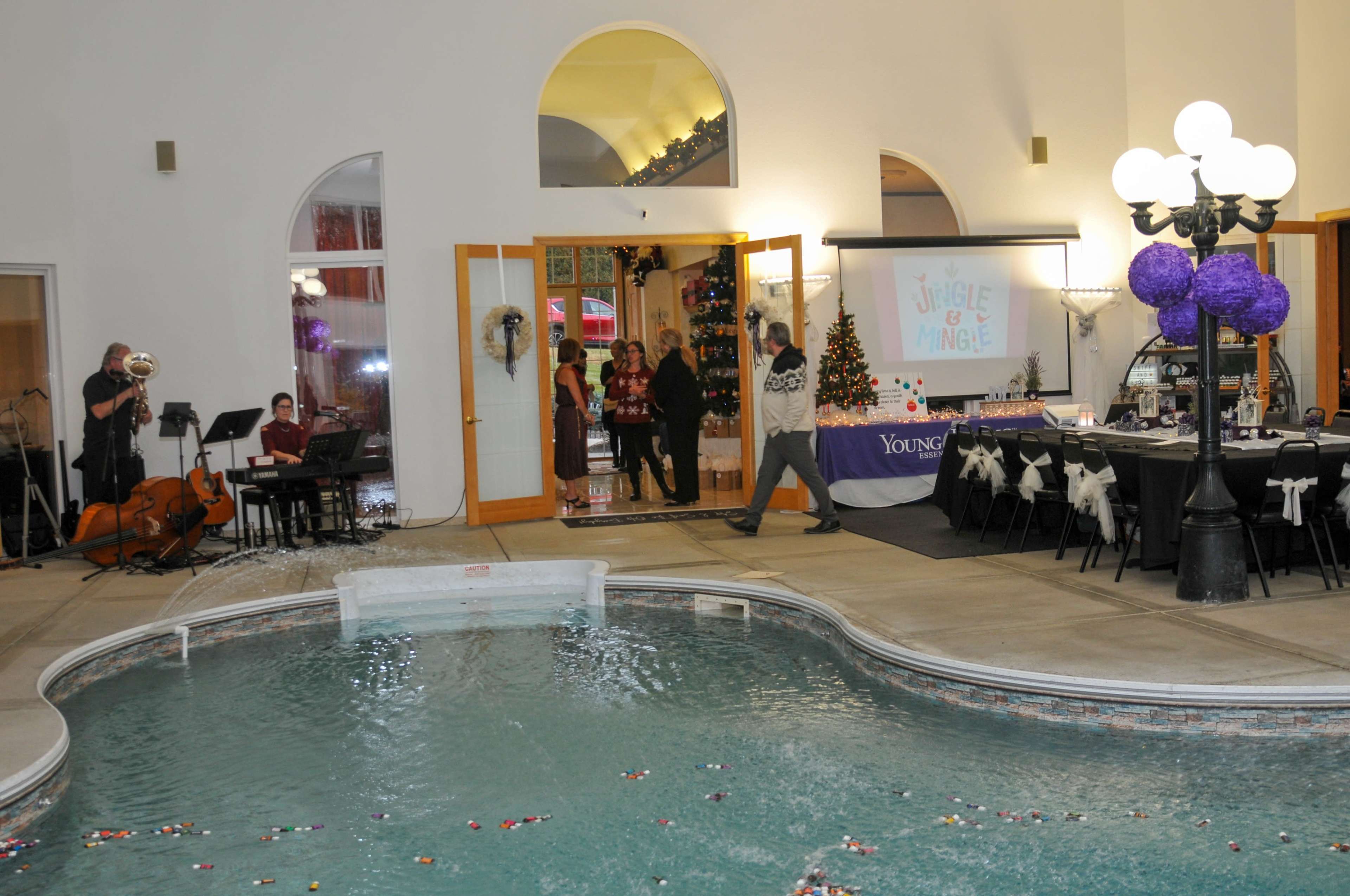 A festive indoor event takes place near a swimming pool, featuring musicians and a decorated dining area.