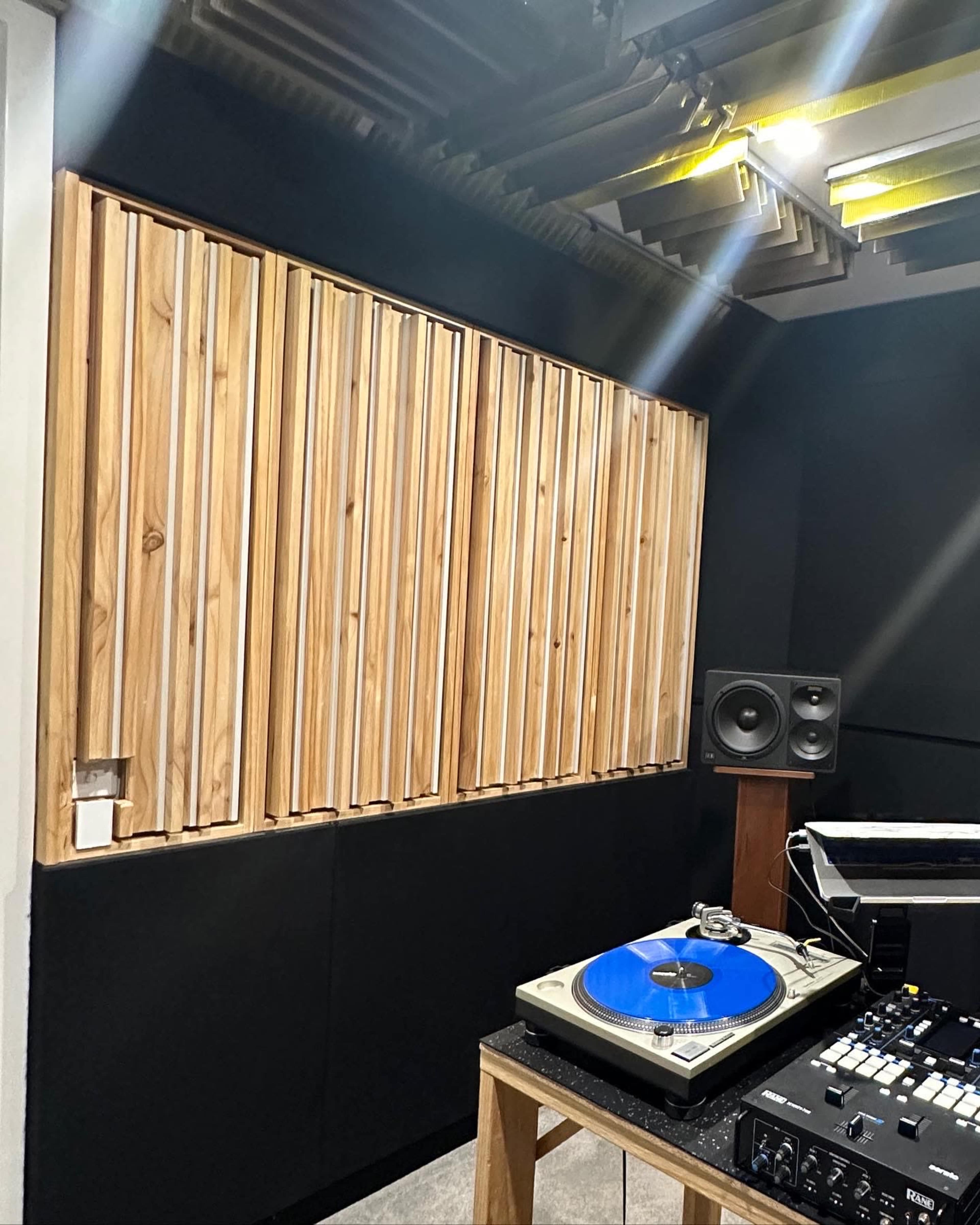 The image shows a recording studio corner with a wooden acoustic panel, a turntable with a blue vinyl record, and a speaker setup.