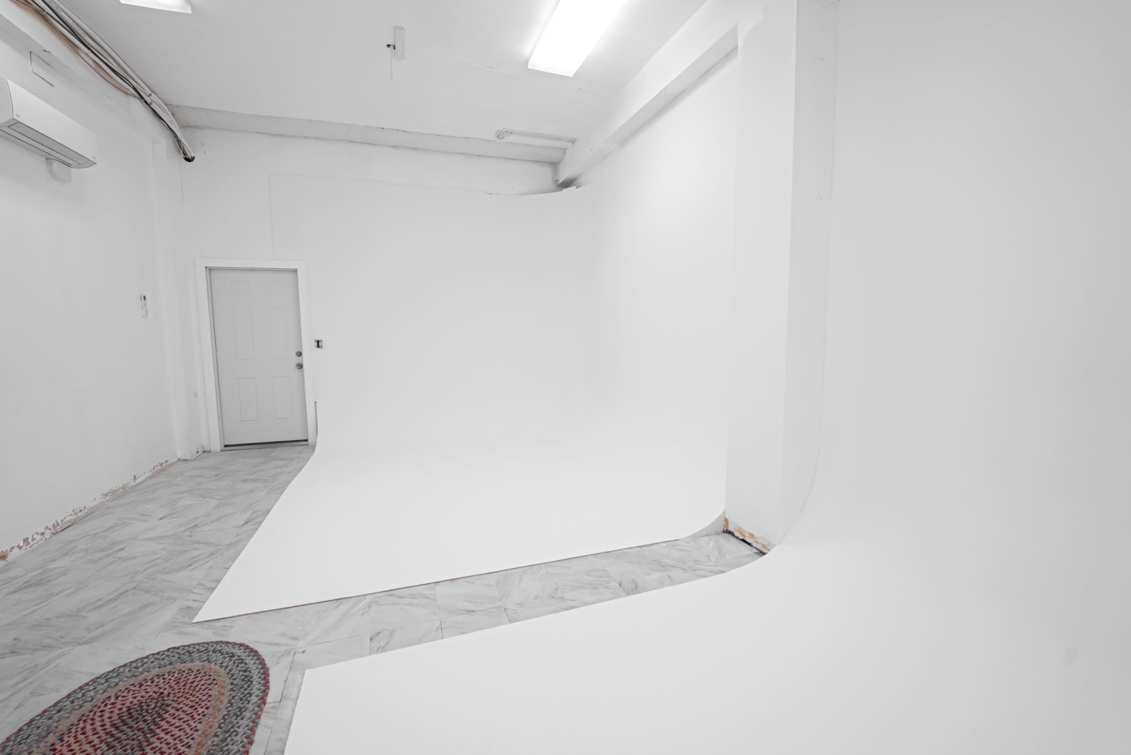 The image shows a spacious, minimalistic studio with white walls and a curved backdrop on the floor.
