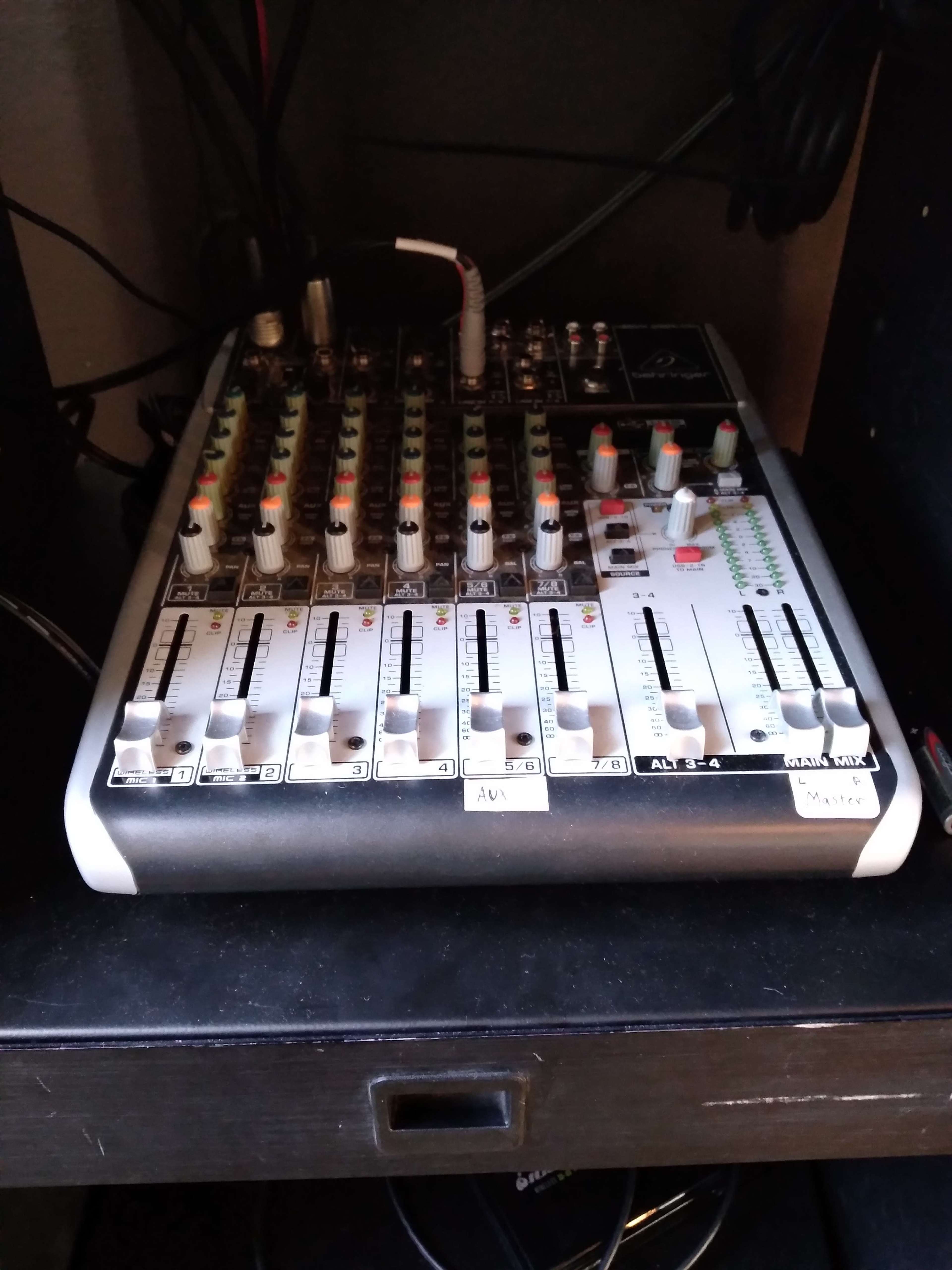 A compact audio mixer with multiple channels and adjustable sliders sits inside a dark cabinet.
