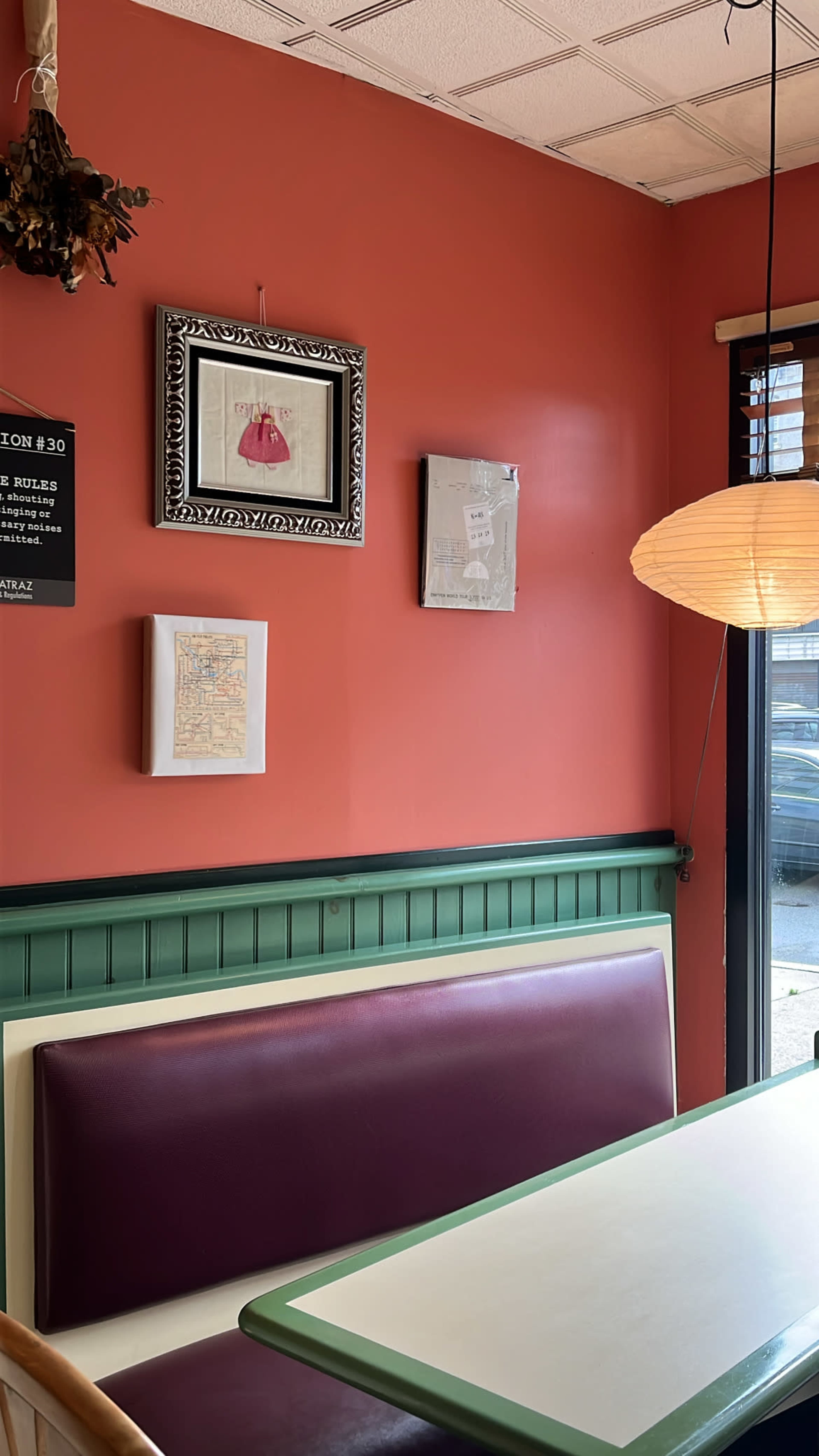 A cozy dining area with a red wall, green wainscoting, and a white and purple booth seating arrangement illuminated by a pendant light.
