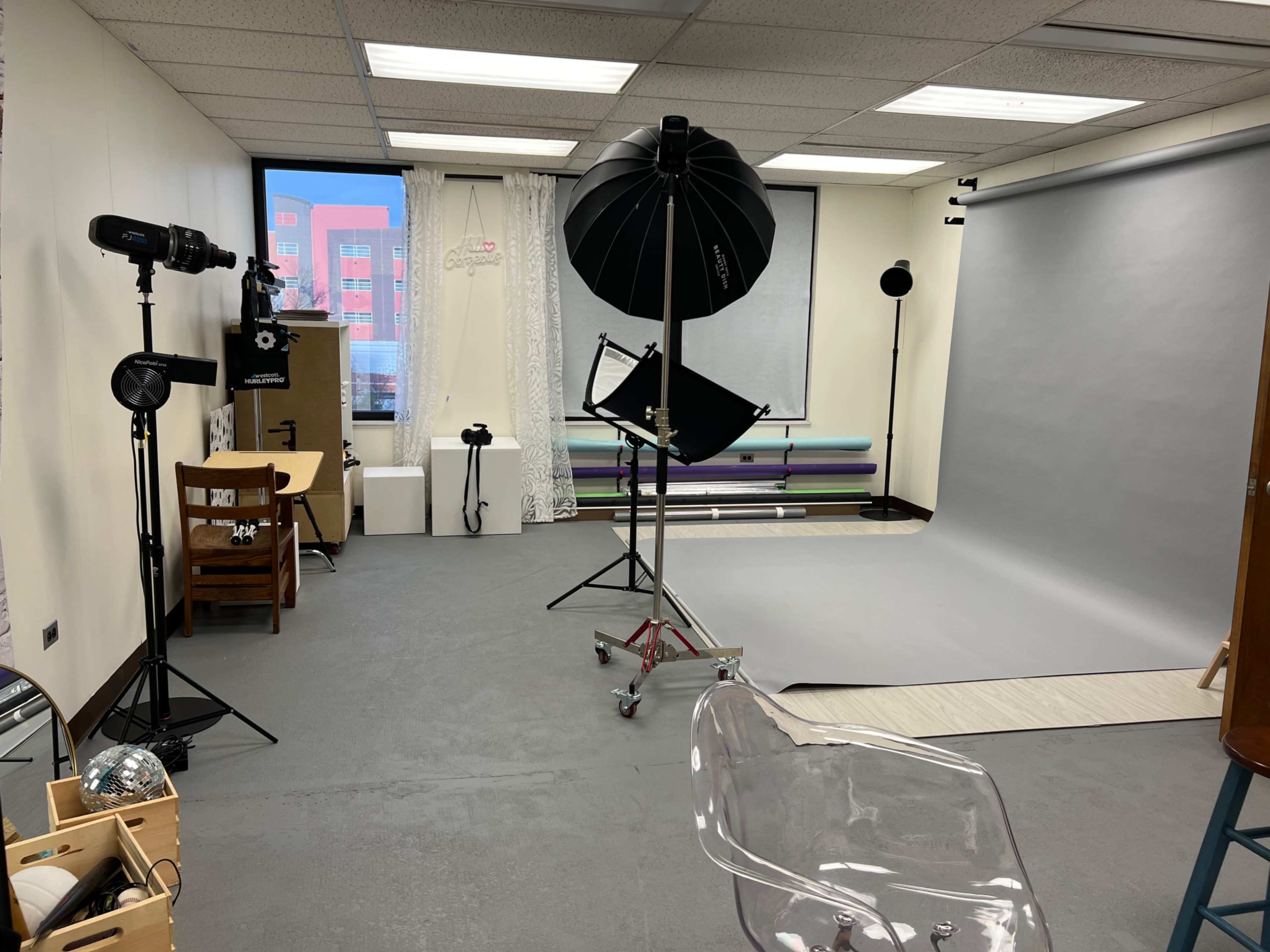 The image shows a photography studio with lighting equipment, a backdrop, and various props arranged in the space.